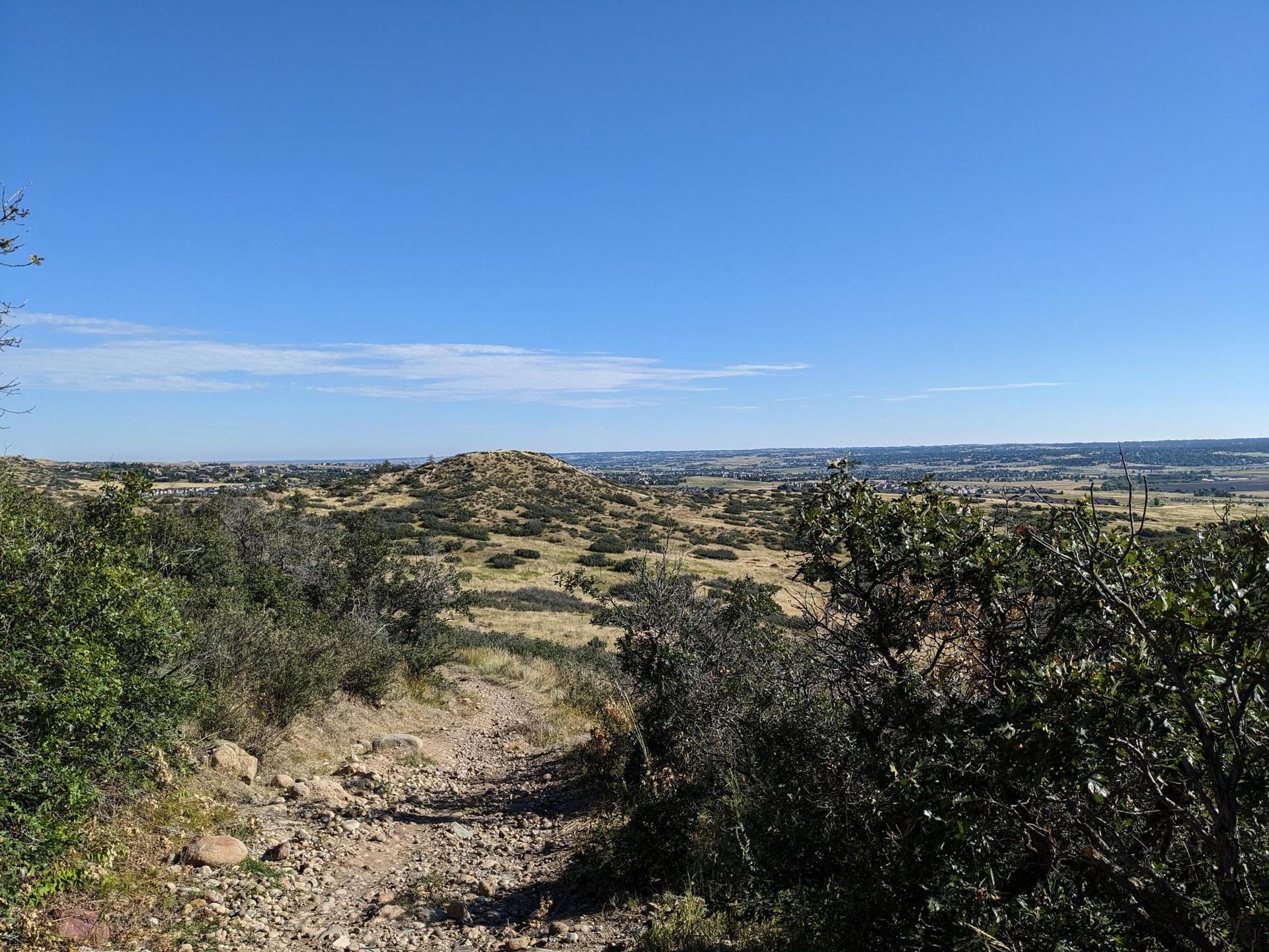 Sunny panoramic view of rolling hills with sparse vegetation under a blue sky.