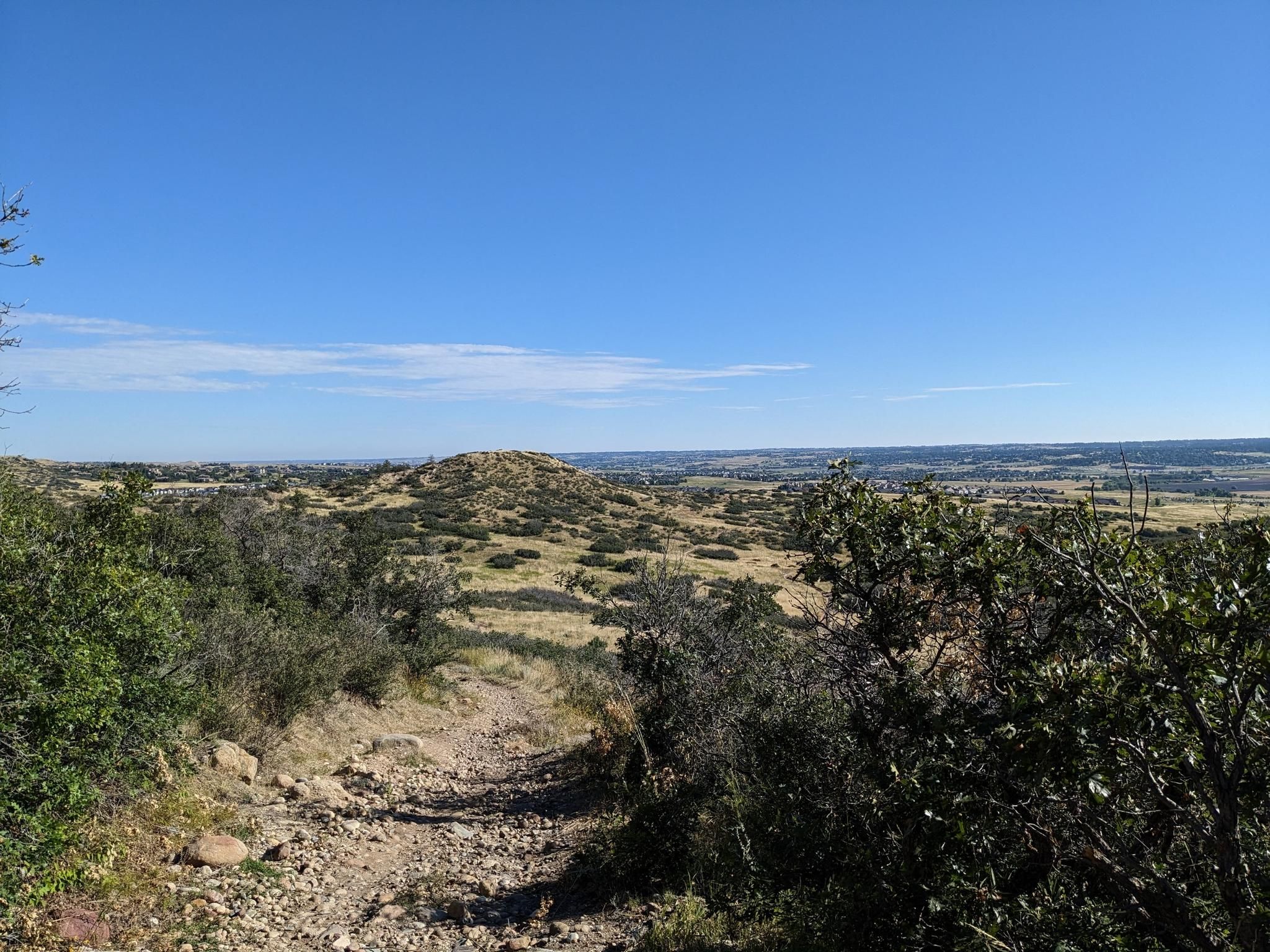 Sunny panoramic view of rolling hills with sparse vegetation under a blue sky. - Hidden Mesa Loop