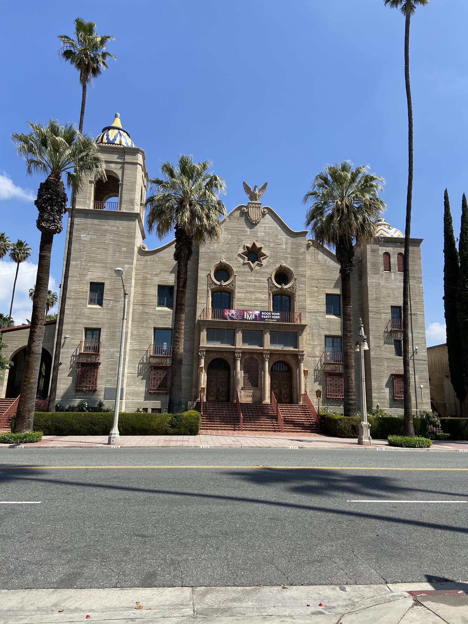 An ornate stone building with towers and palm trees under a bright blue sky.