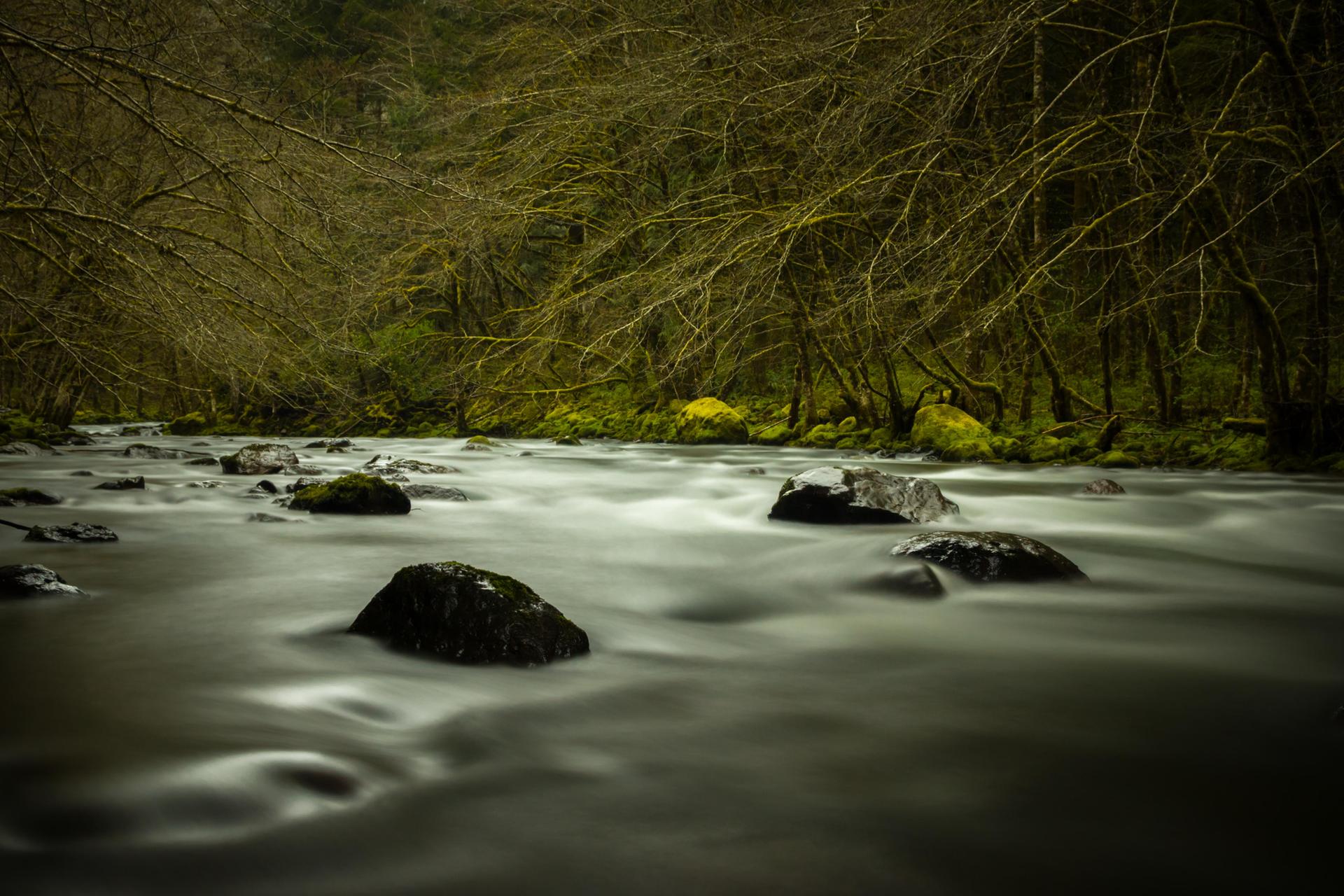 Moody long exposure of a river with blurred water and dark rocks.