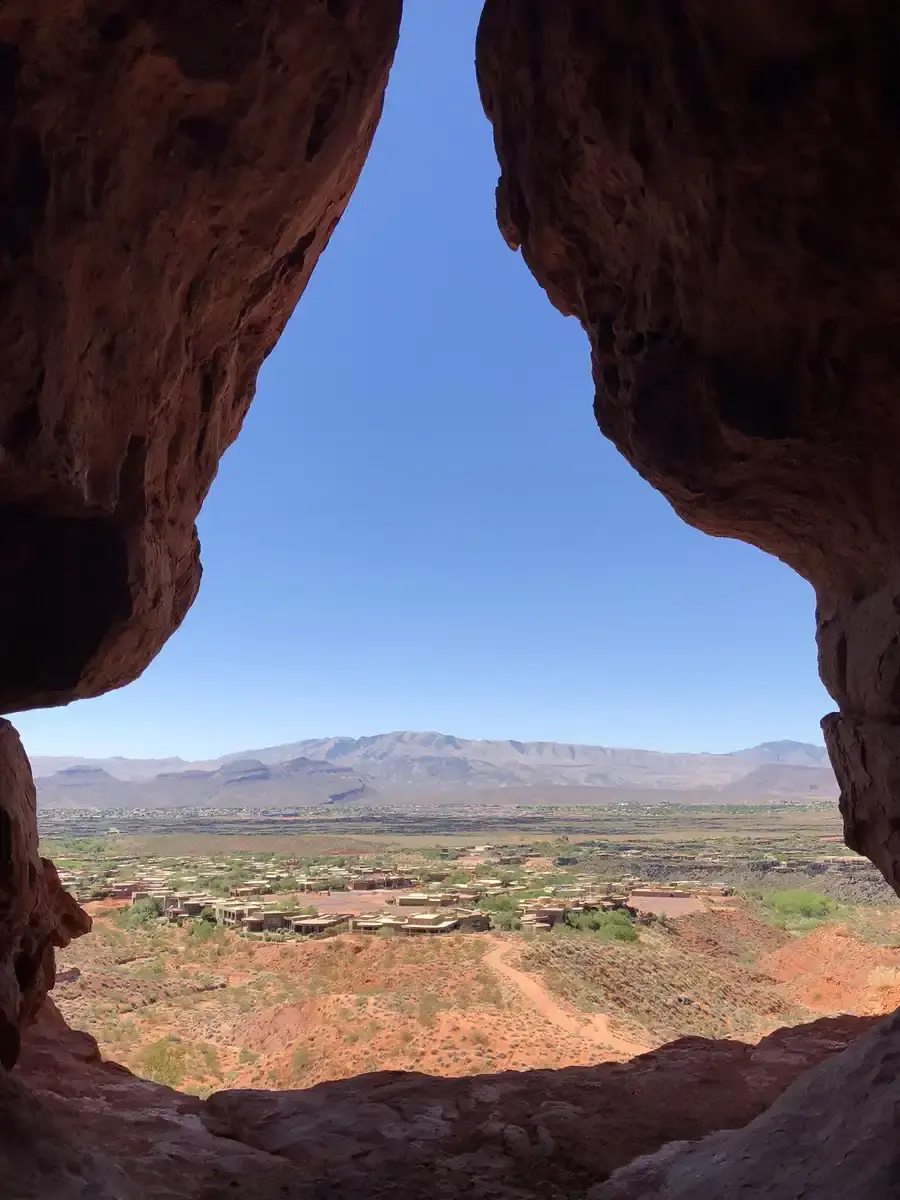 View through a rock opening of a sunny desert valley and distant mountains.