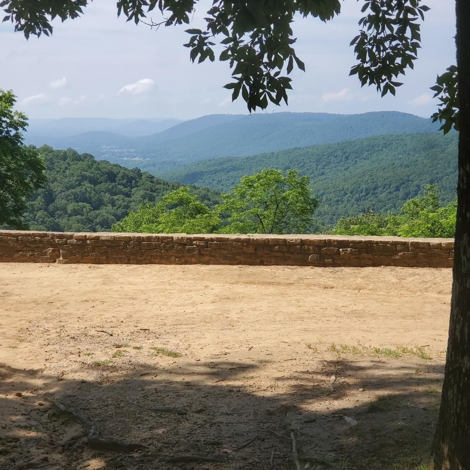 Bright view of distant green mountains over a stone wall and dirt.