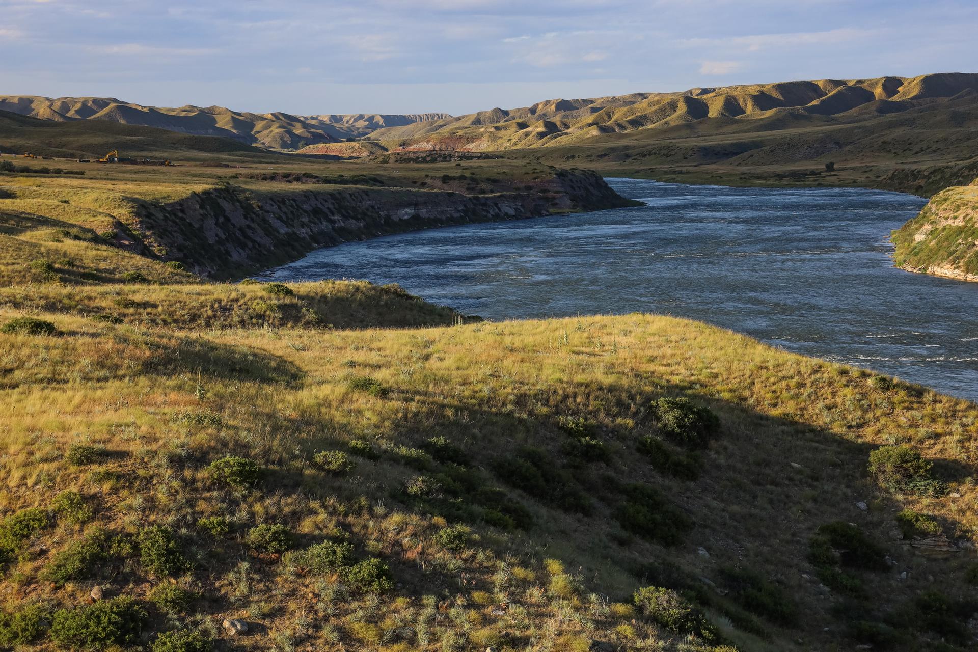 Wide river flows through grassy hills under golden light.