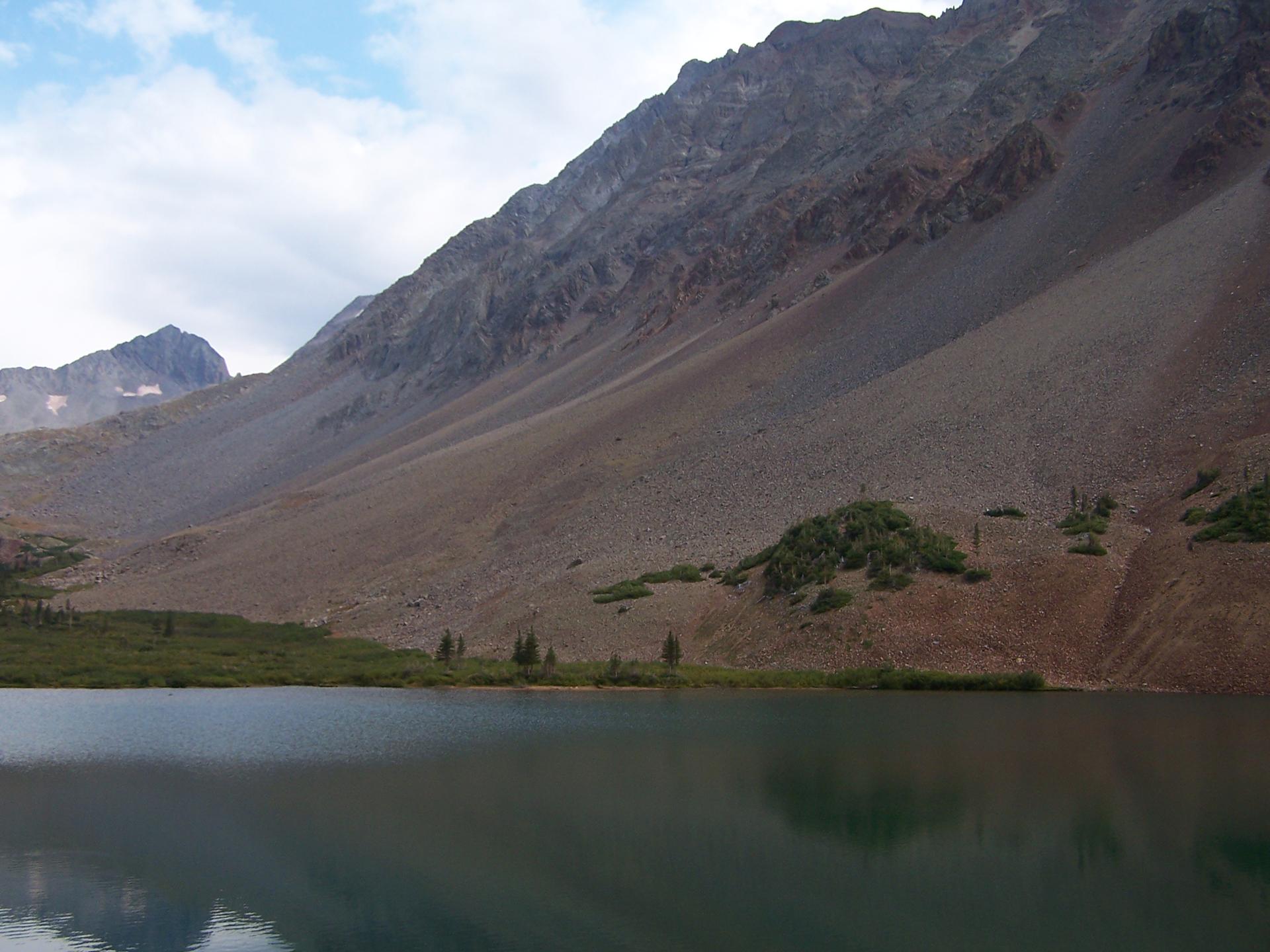 Dark mountain lake with steep, rocky slopes under an overcast sky.