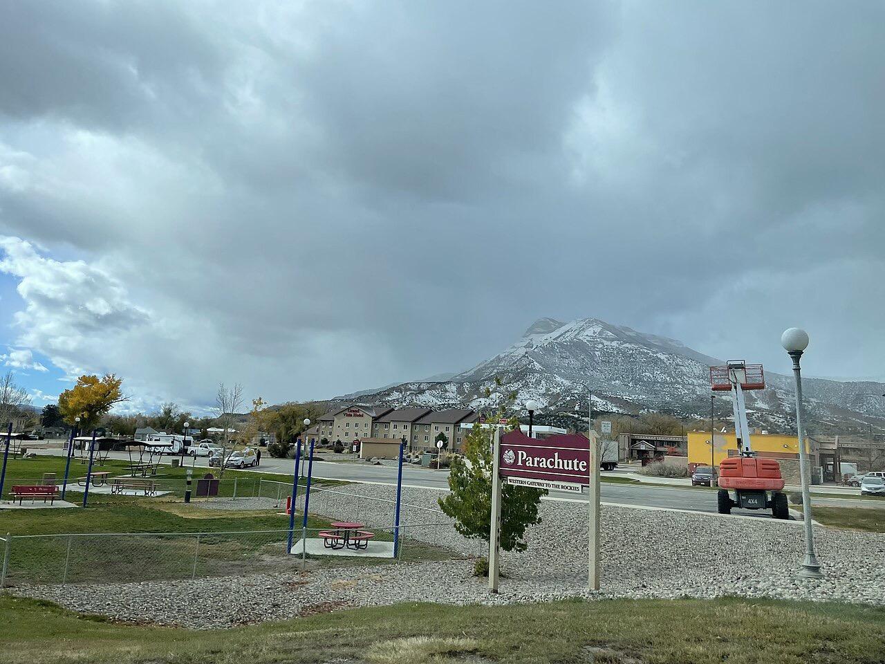 A cloudy sky over a snow-dusted mountain behind a small town park.