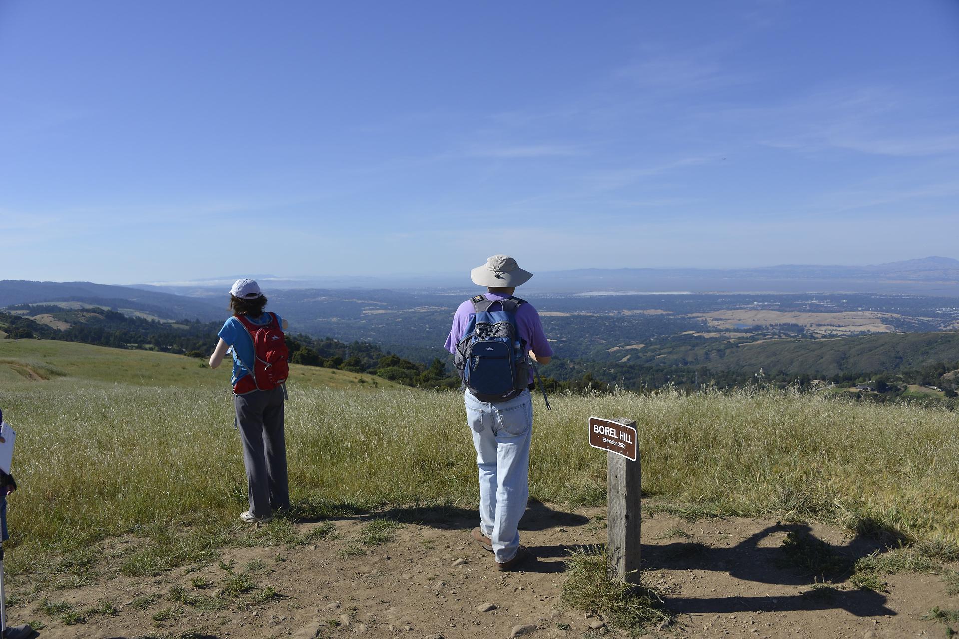 Two hikers on a hilltop overlooking a valley under a clear sky.
