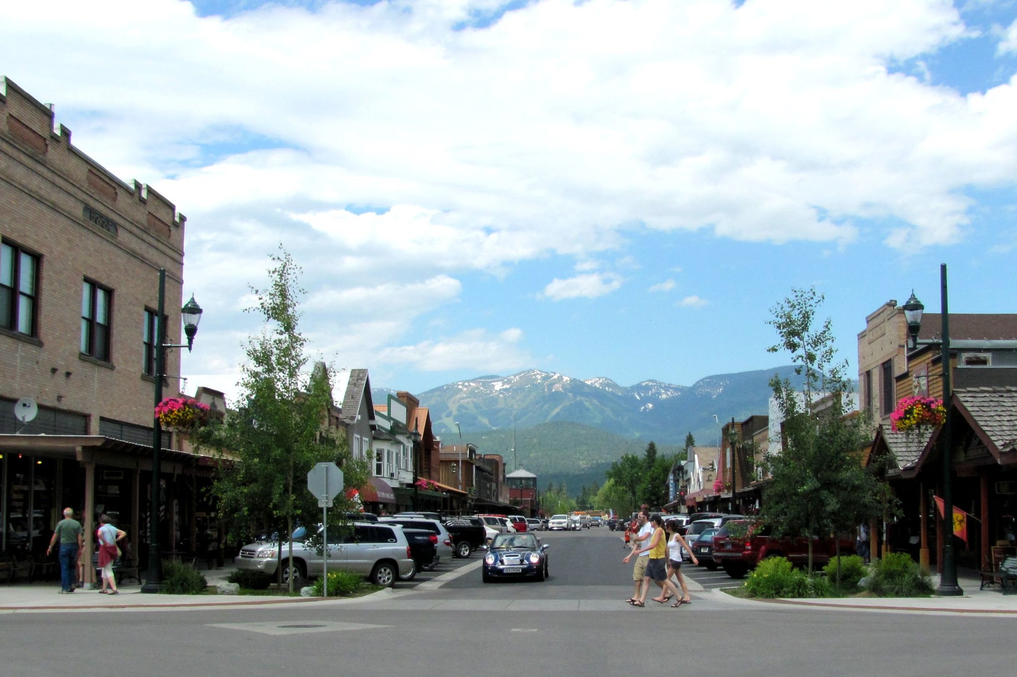 Bustling town street with people, buildings, and distant mountains under blue sky. - Great Northern Railway Depot – Historic Whitefish loop from Whitefish