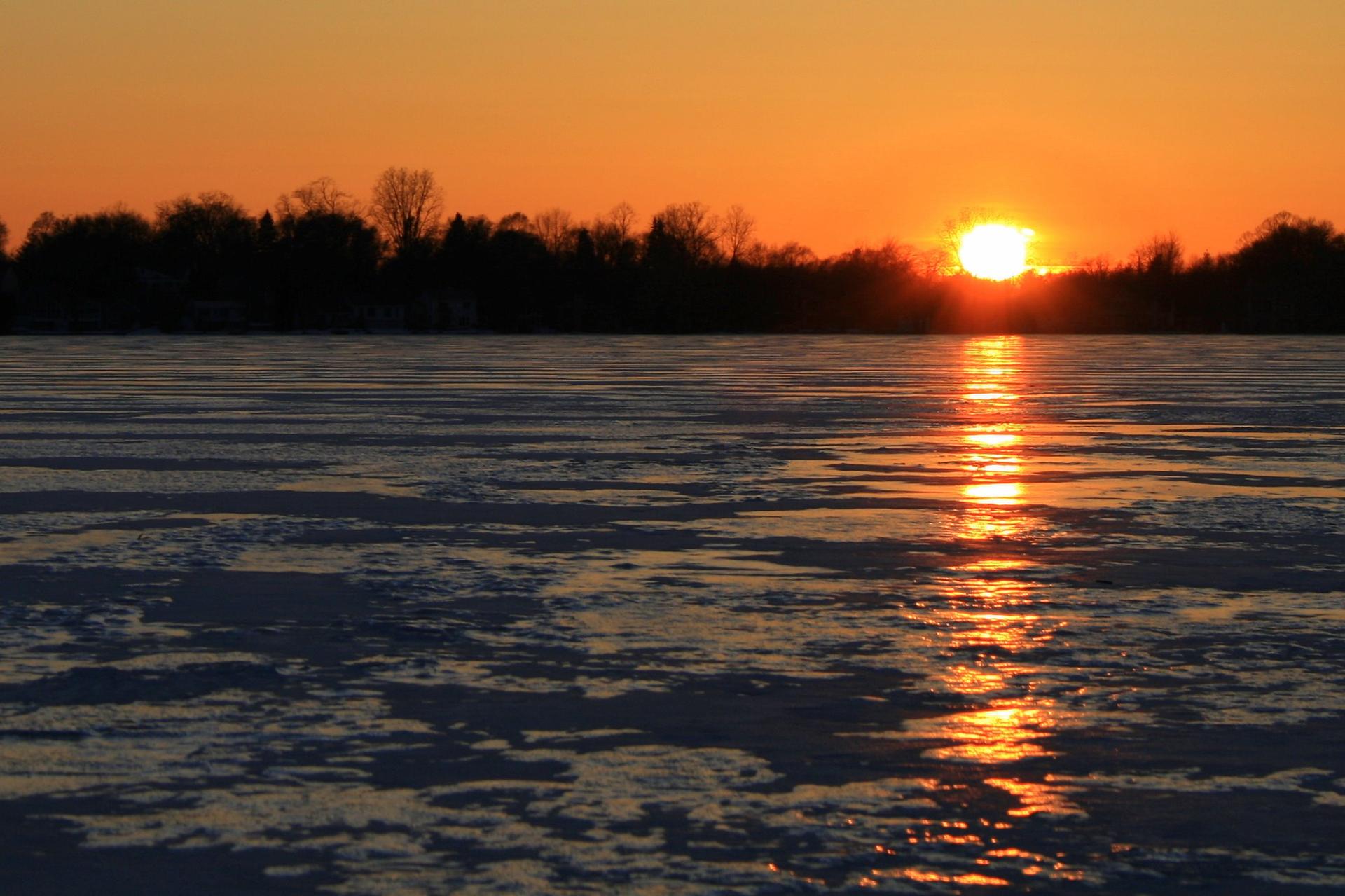 Golden sunset over a partially frozen lake with silhouetted trees.