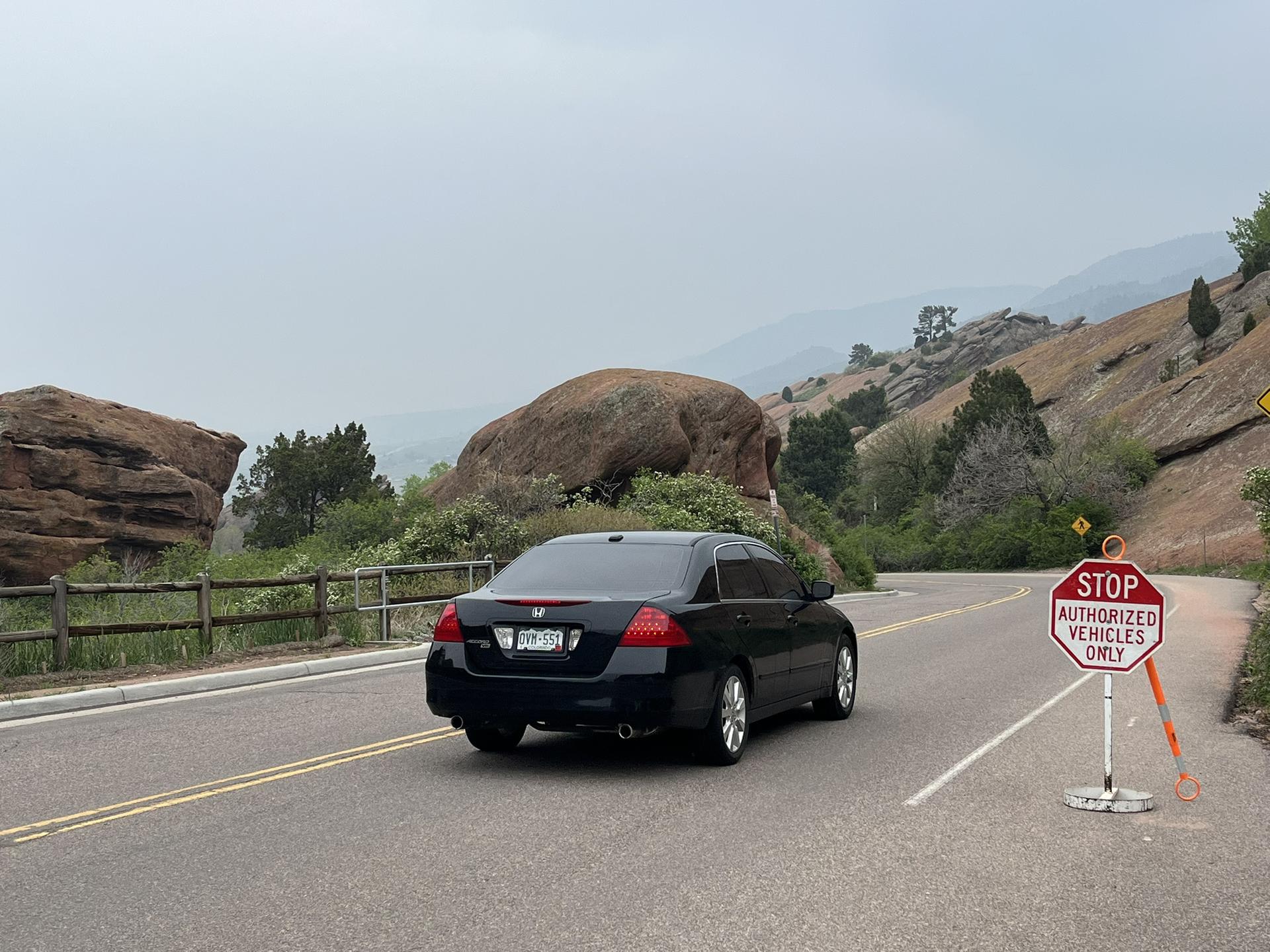A black car drives on a winding road past large rock formations.