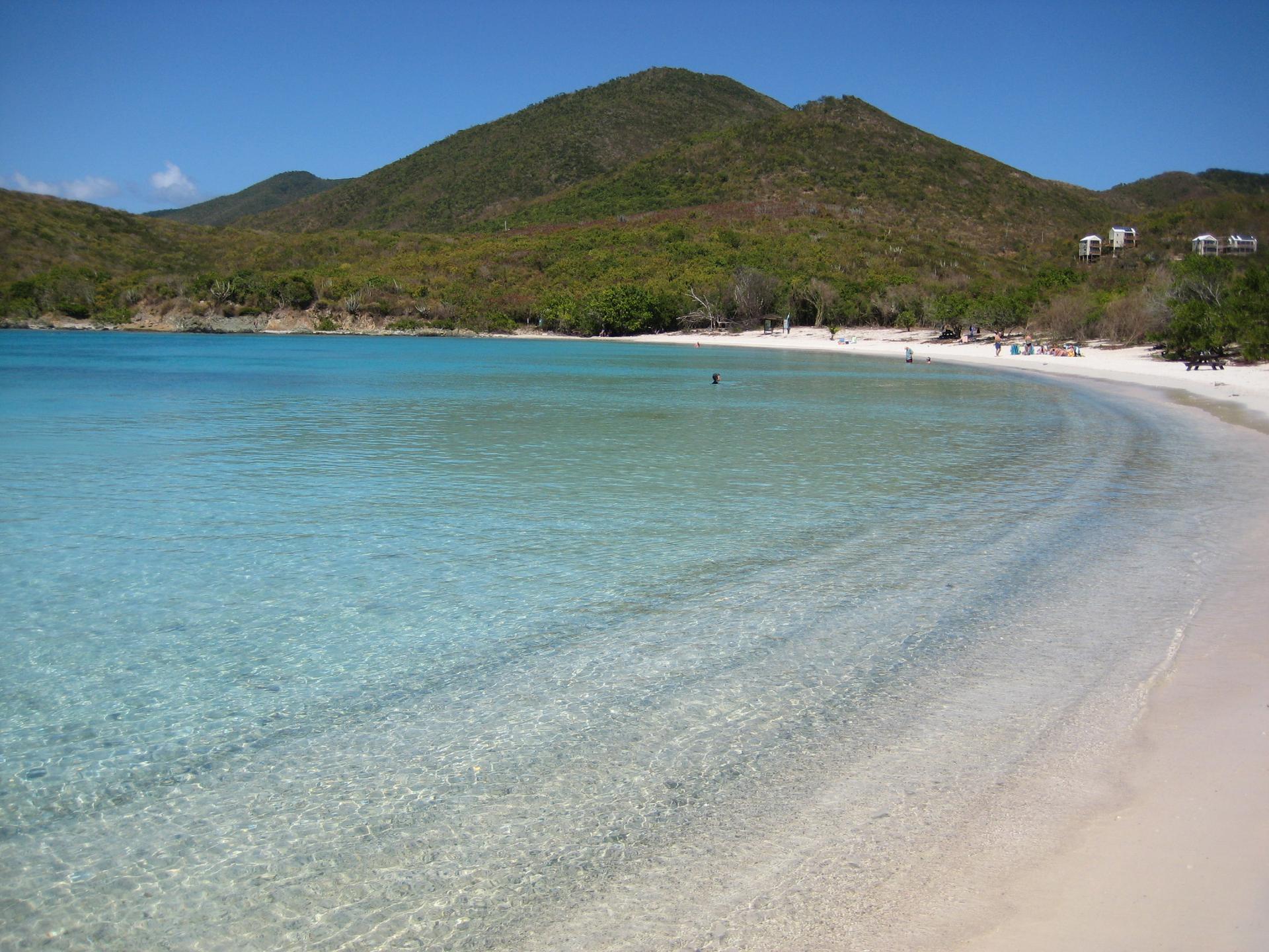 Pristine sandy beach with clear turquoise water and lush green hills.