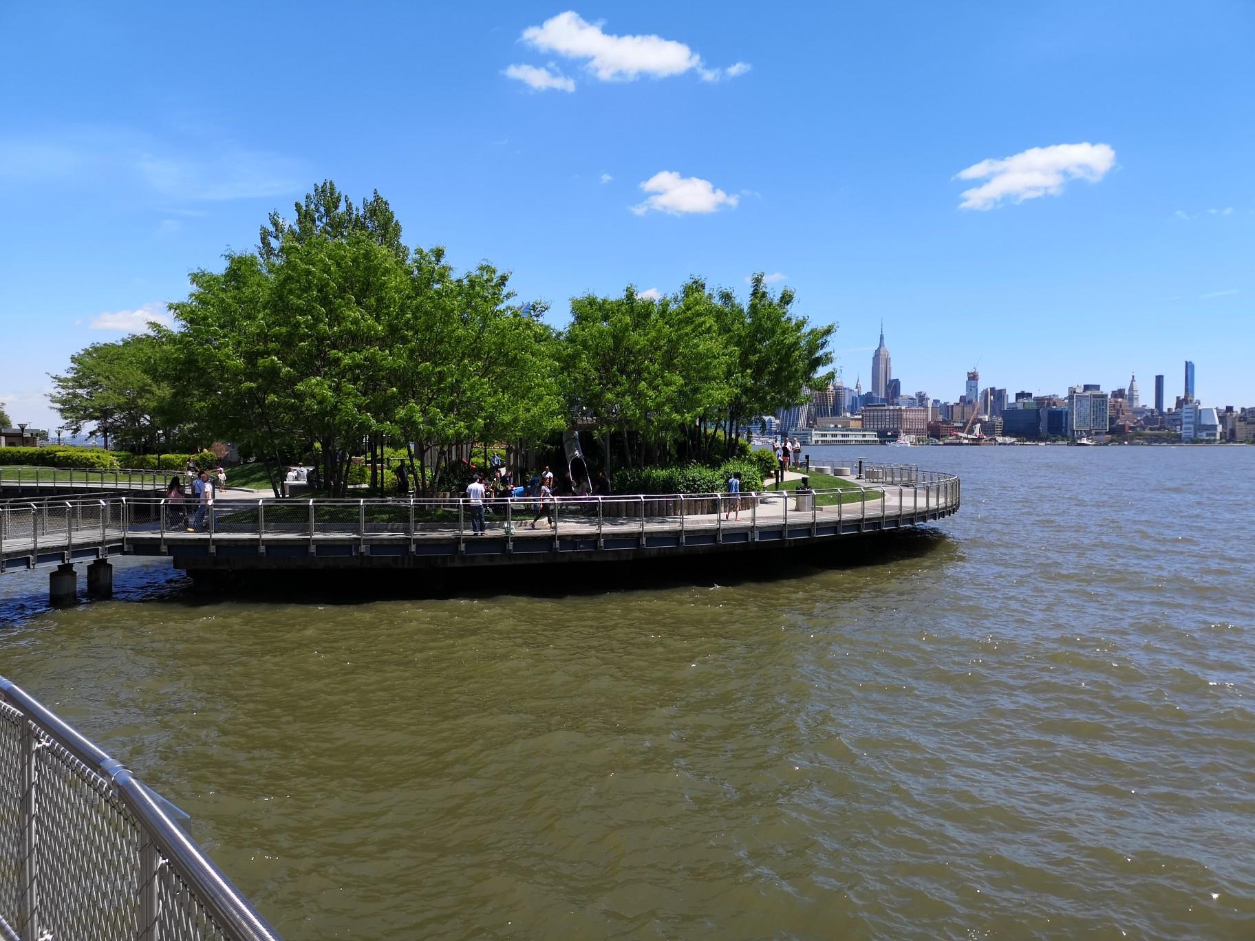 People on a circular pier with trees, overlooking a distant city skyline.