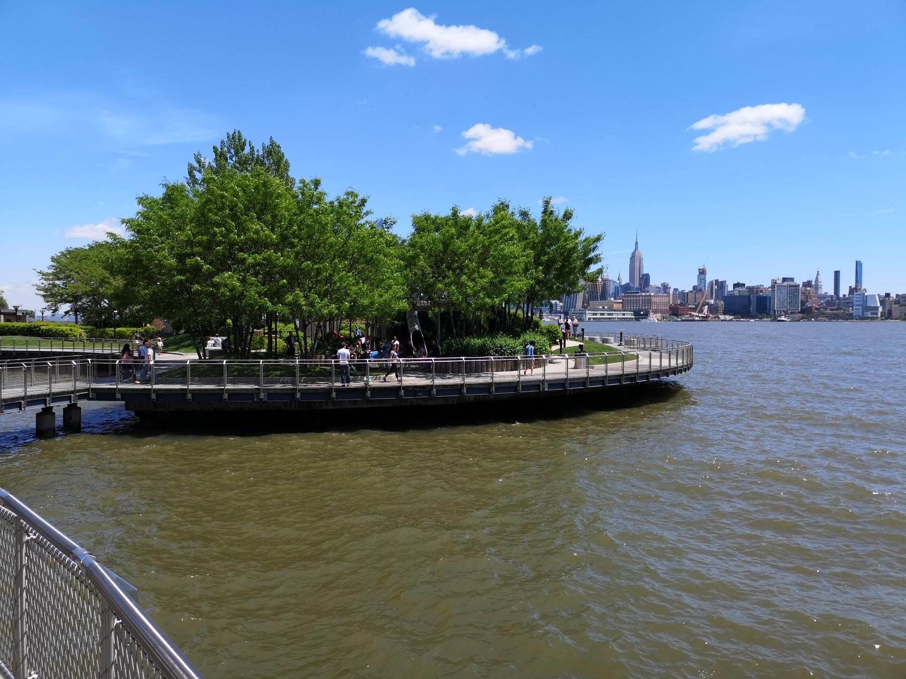People on a circular pier with trees, overlooking a distant city skyline. - Hoboken Terminal – Weehawken Cove loop from 2nd Street