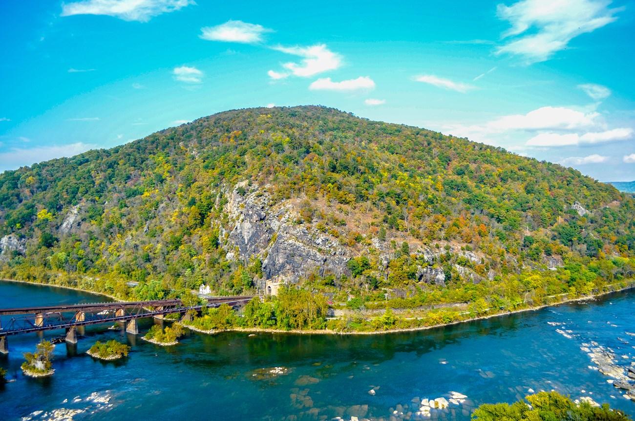 Aerial view of a large forested mountain, river confluence, and a long bridge.