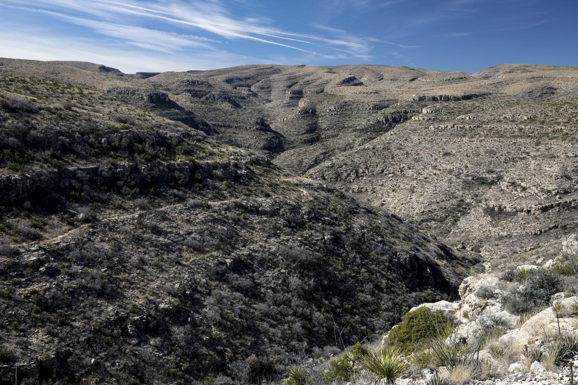 Arid, rocky mountain landscape with a deep canyon under a bright sky.