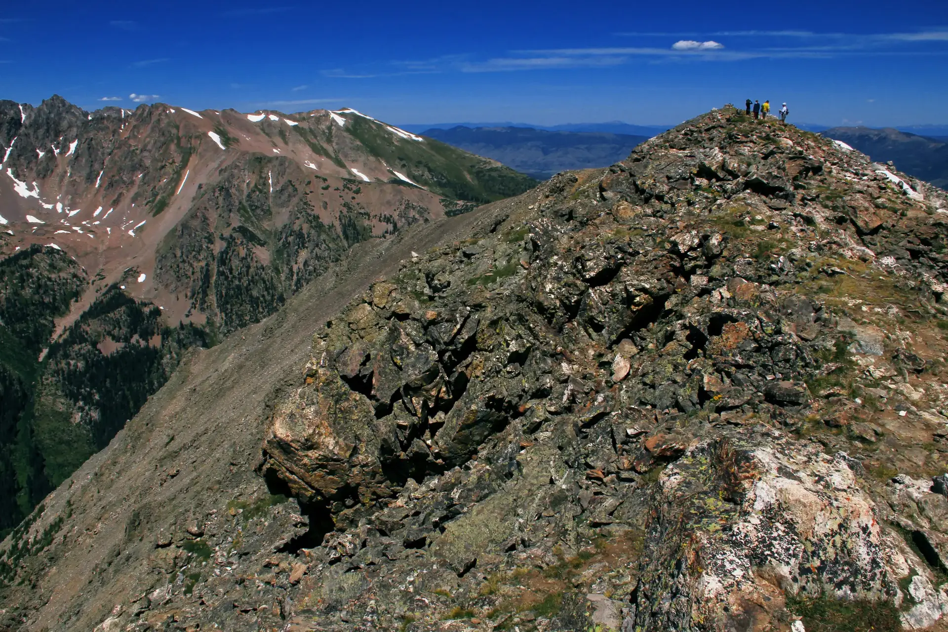 Group of hikers on a rocky mountain peak under a clear blue sky.