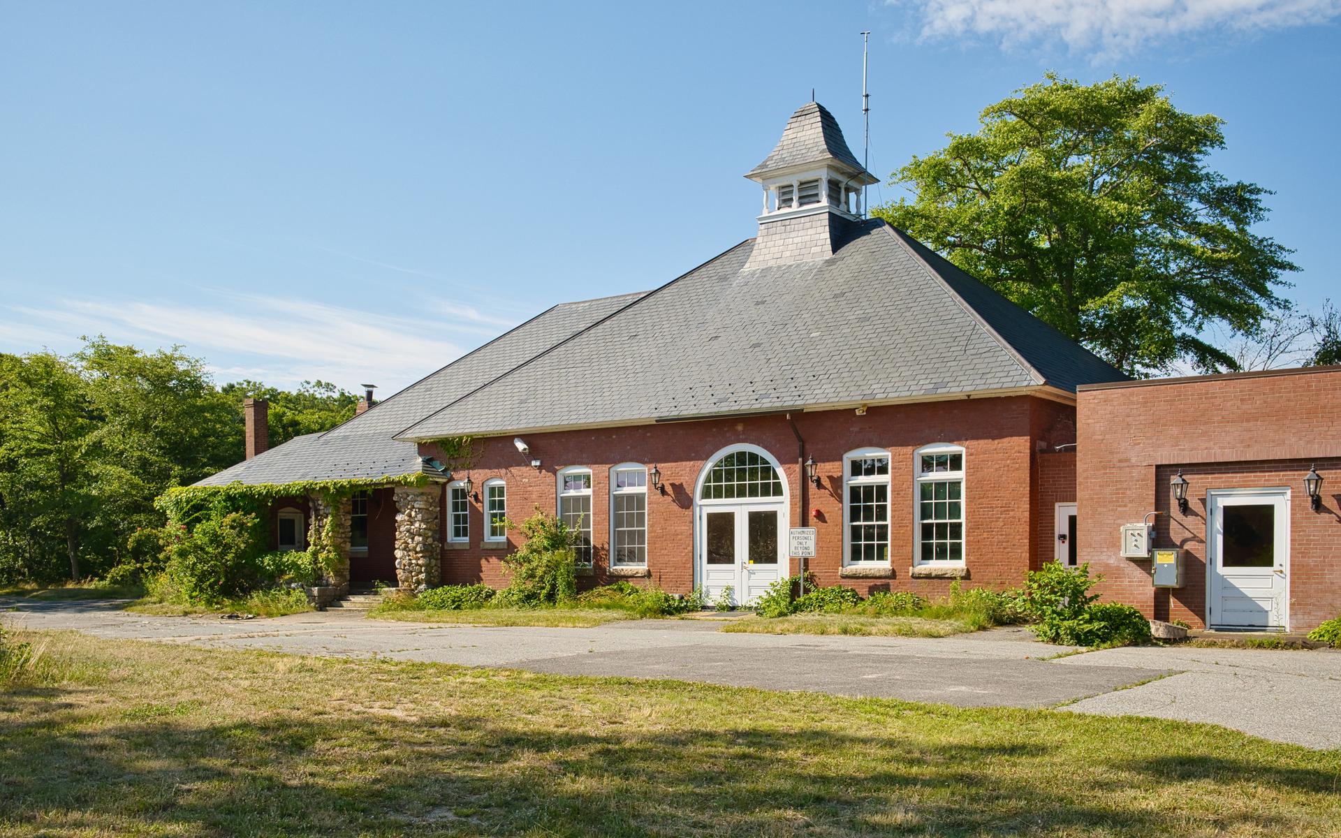 Large brick building with a cupola on a sunny day, surrounded by trees.