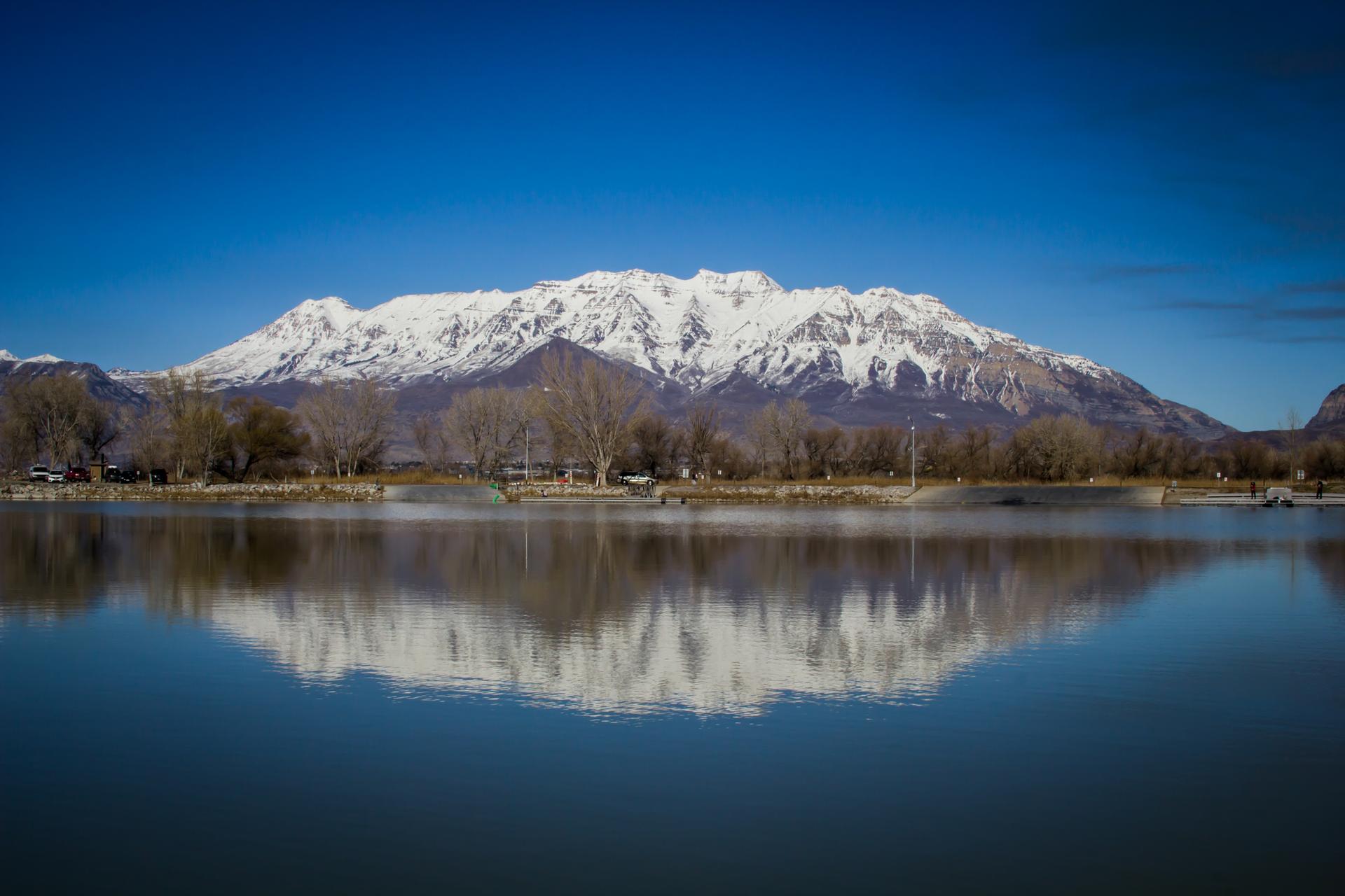 Snow-capped mountains reflect perfectly in a calm lake under a clear blue sky.