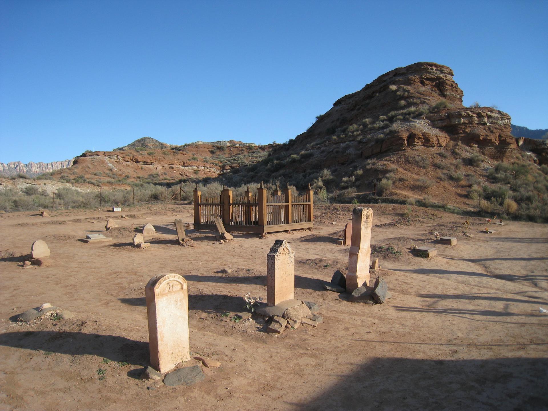 Old gravestones and a wooden fence in a sunny, arid desert landscape.