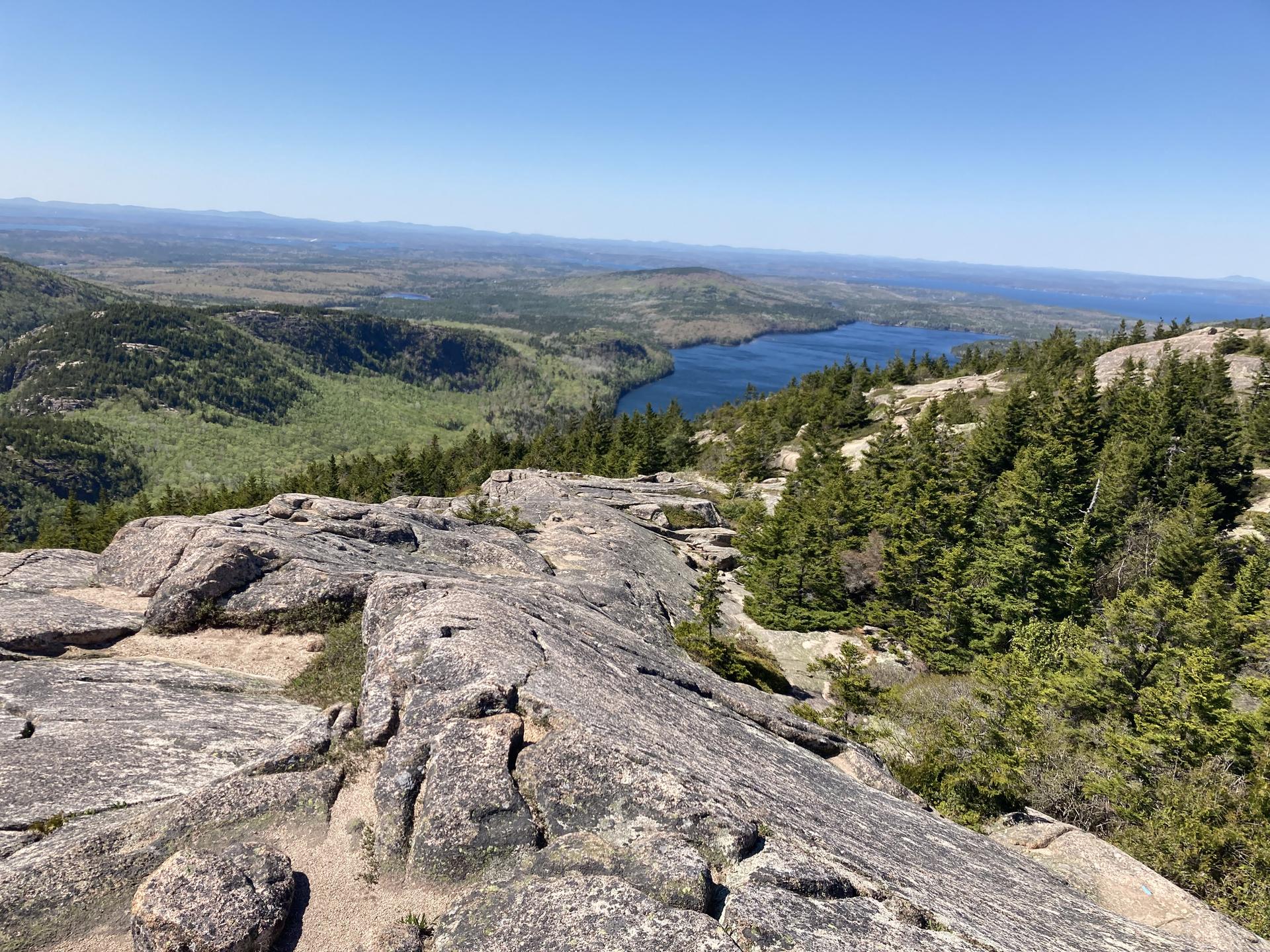 Bright sunny day, rocky foreground overlooking a valley with a lake and distant ocean.