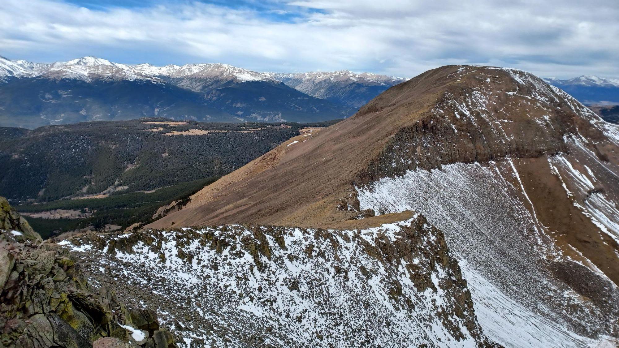 Snow-dusted mountain peaks and a forested valley under a cloudy sky.