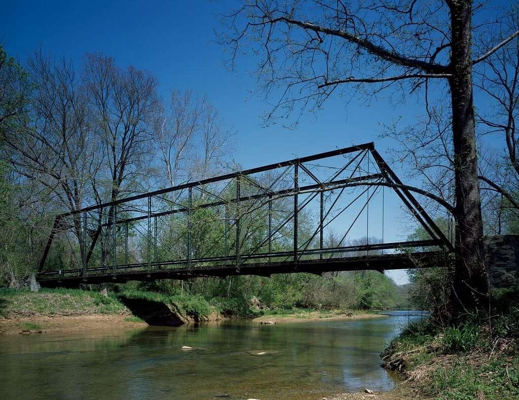 Historic metal truss bridge spans a calm river under a clear blue sky.