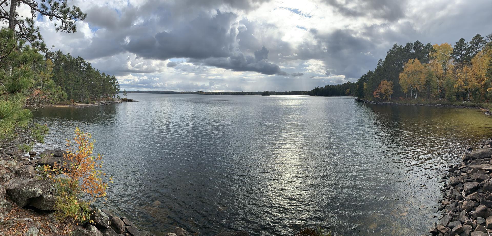 A wide lake surrounded by autumn forests under a cloudy sky.