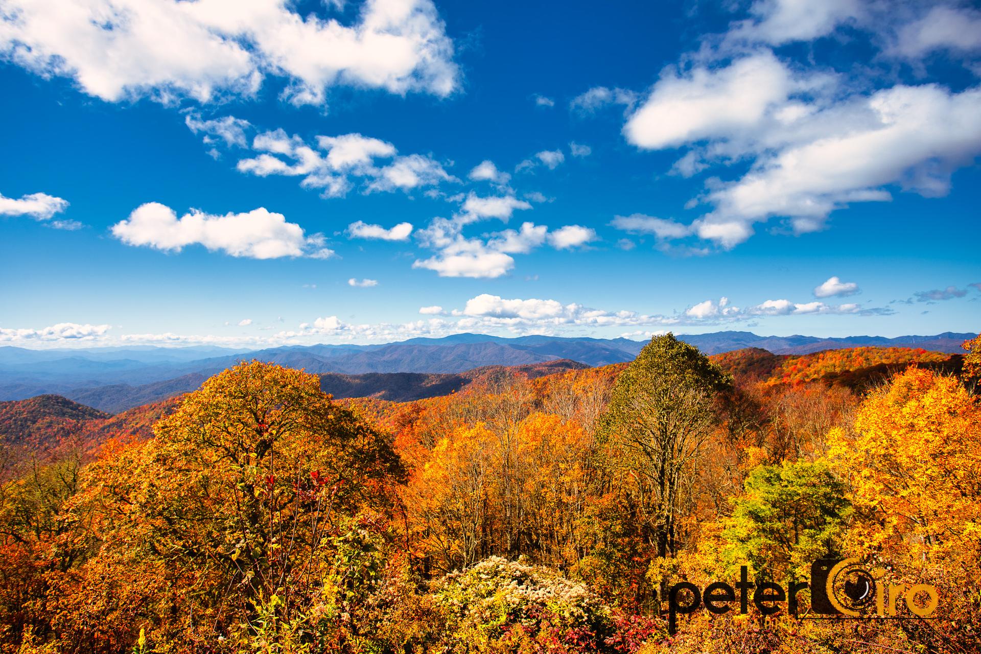 Vibrant autumn foliage covers rolling mountains under a bright blue sky.