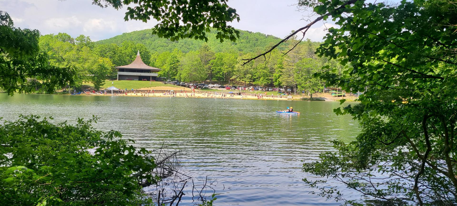 A lake with a distant beach, building, and a kayaker under a bright sky.