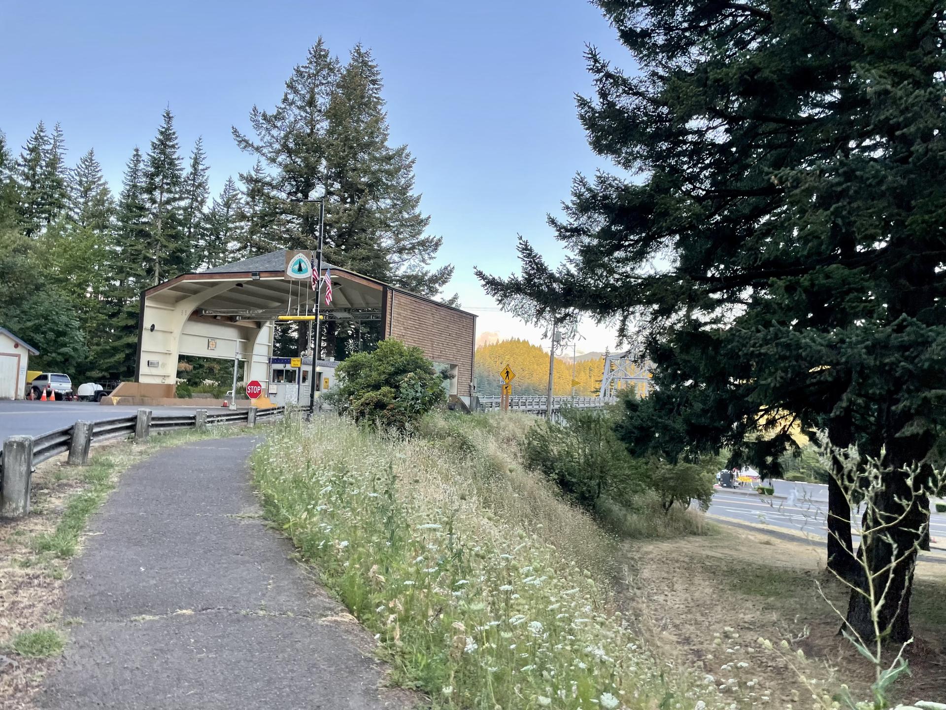 A paved path leads to a building with an awning, surrounded by trees.