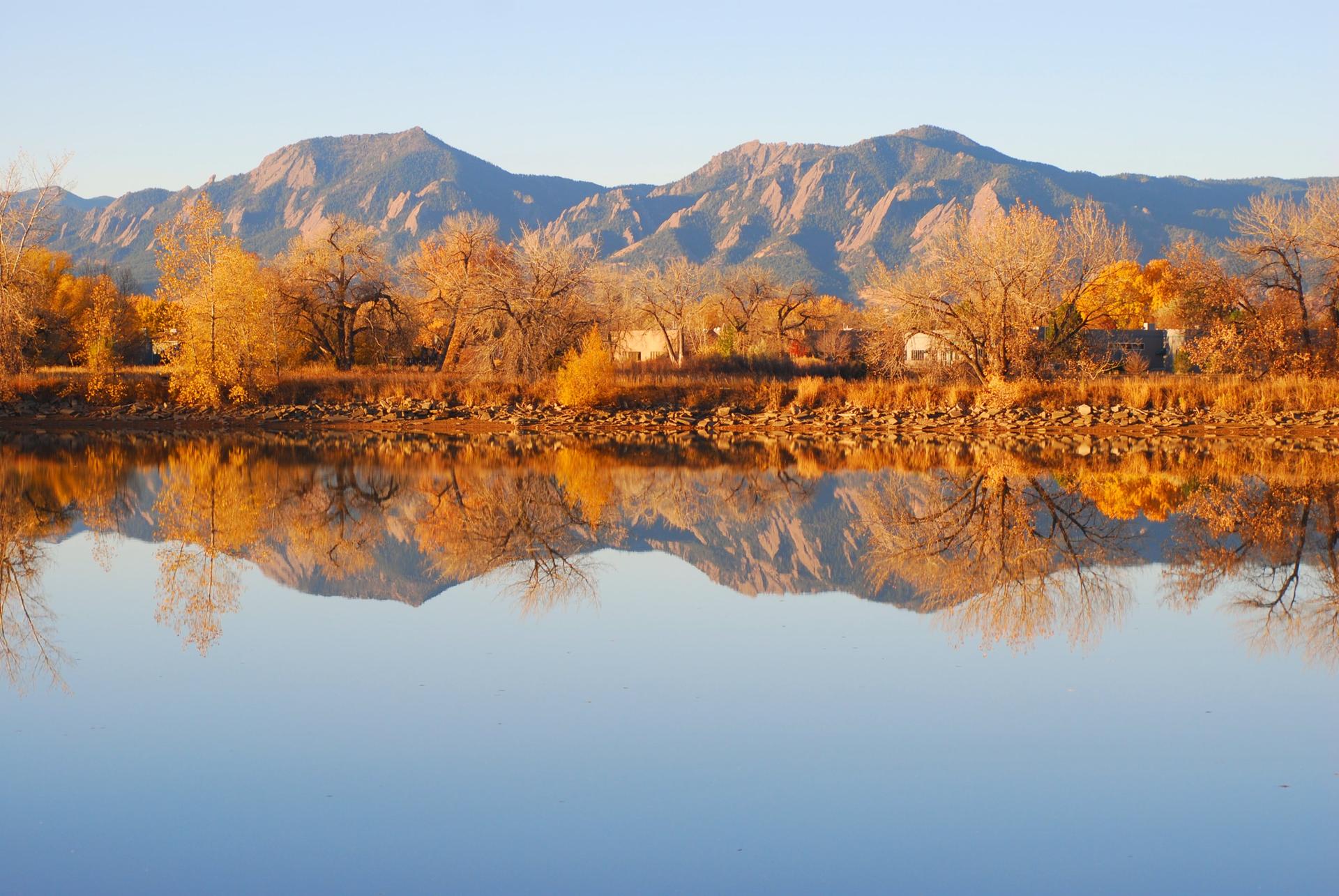 Golden autumn trees and mountains reflect perfectly in still water.
