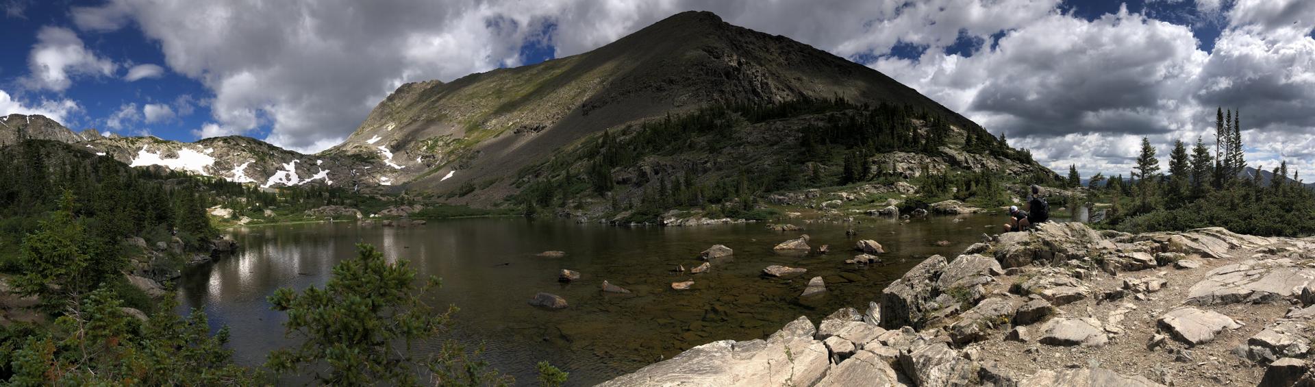 Panoramic view of a mountain lake, rocky shore, and cloudy sky.