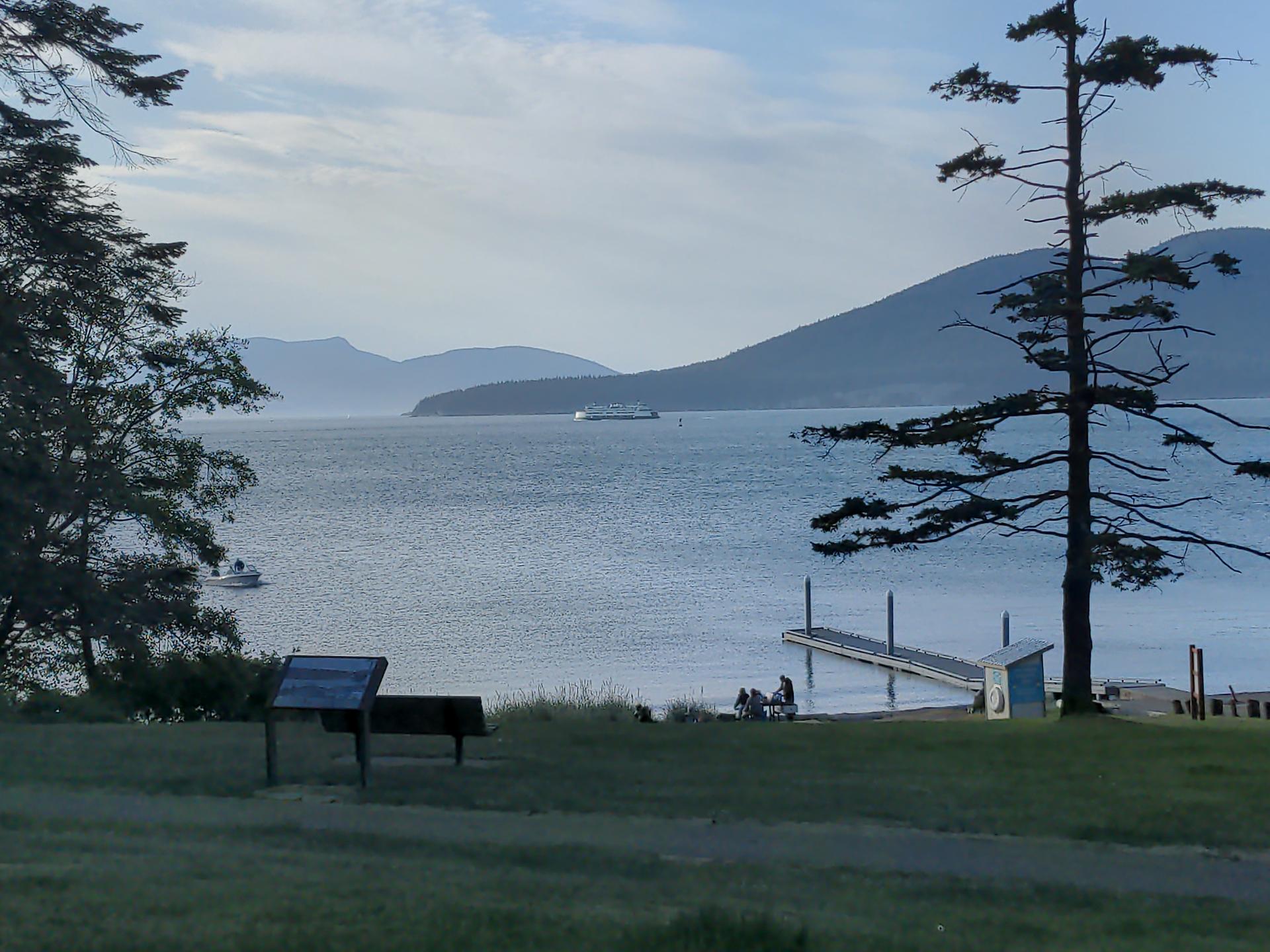 Serene bay with distant mountains, a dock, and people at dusk.