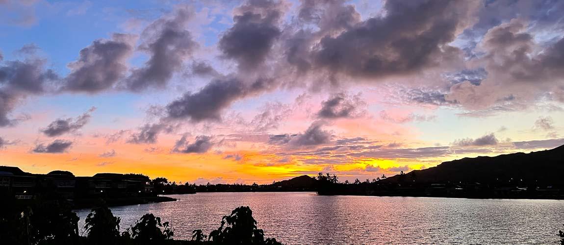 Vibrant sunset over a calm lake with silhouetted hills and clouds.