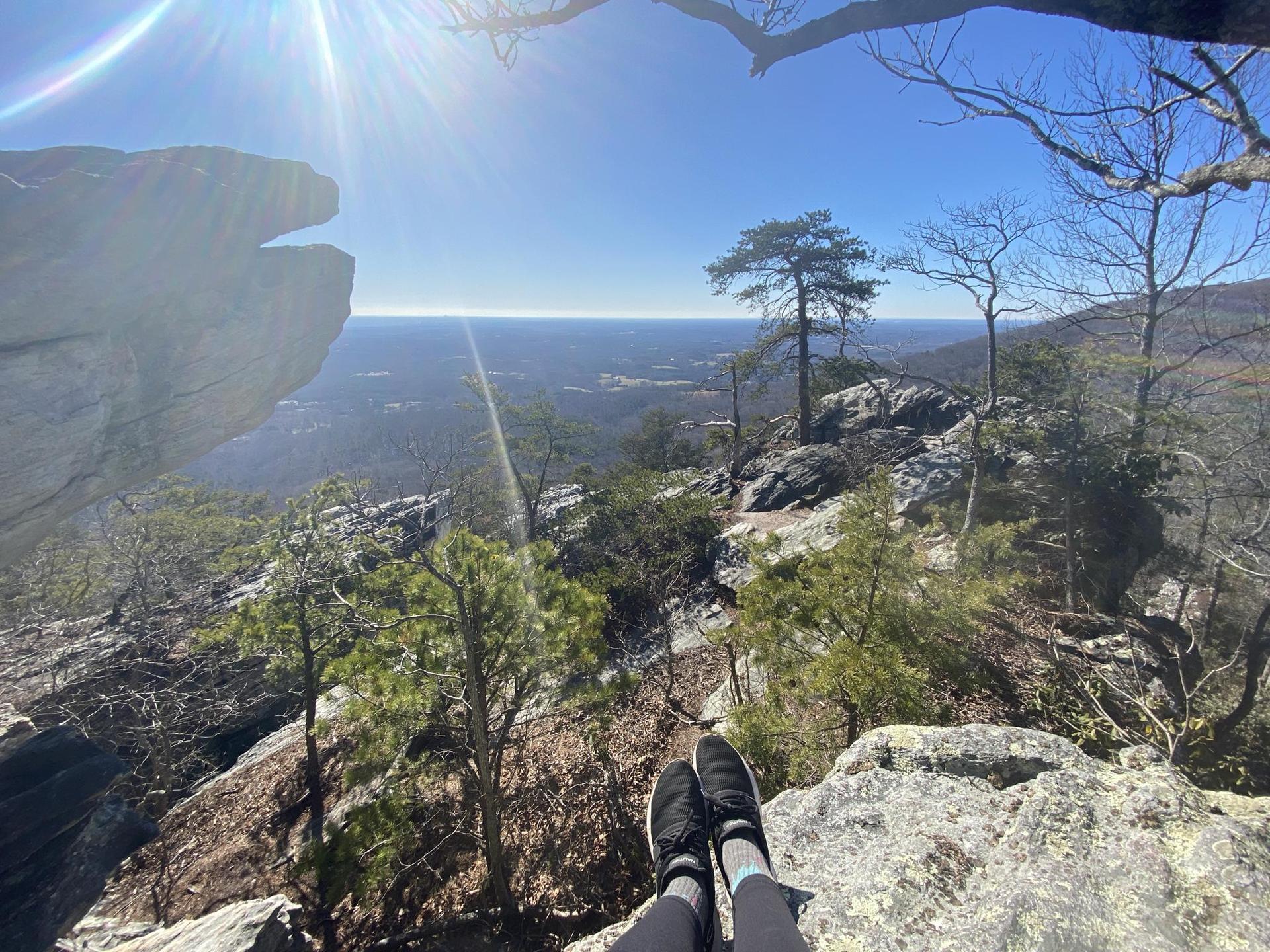 Person's feet on a rocky cliff overlooking a vast sunny landscape.