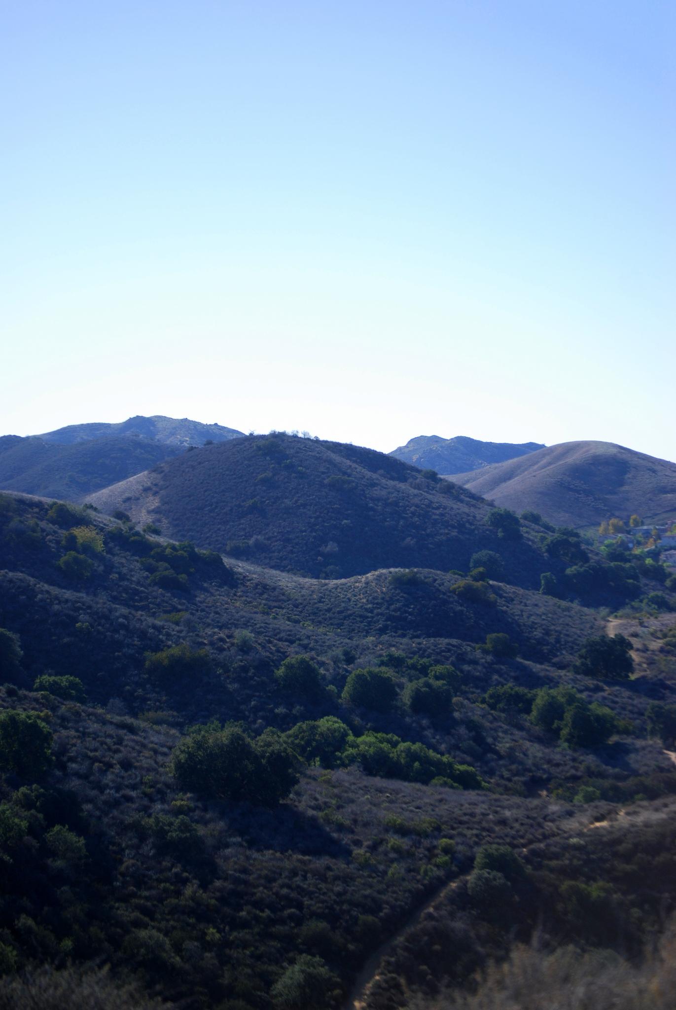 Rolling hills covered in green and brown vegetation under a clear blue sky.