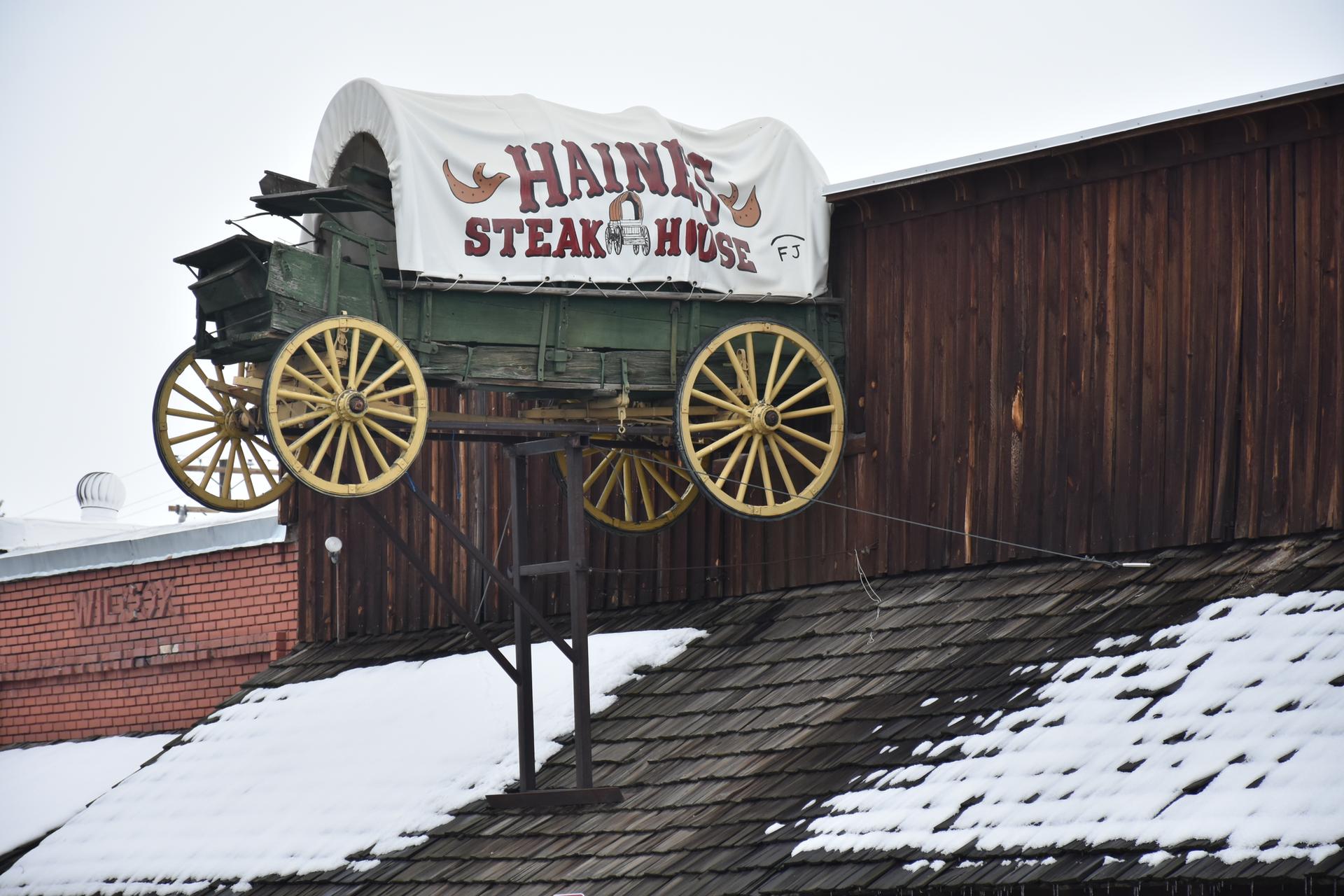 An old covered wagon sign on a wooden building with a snow-covered roof.