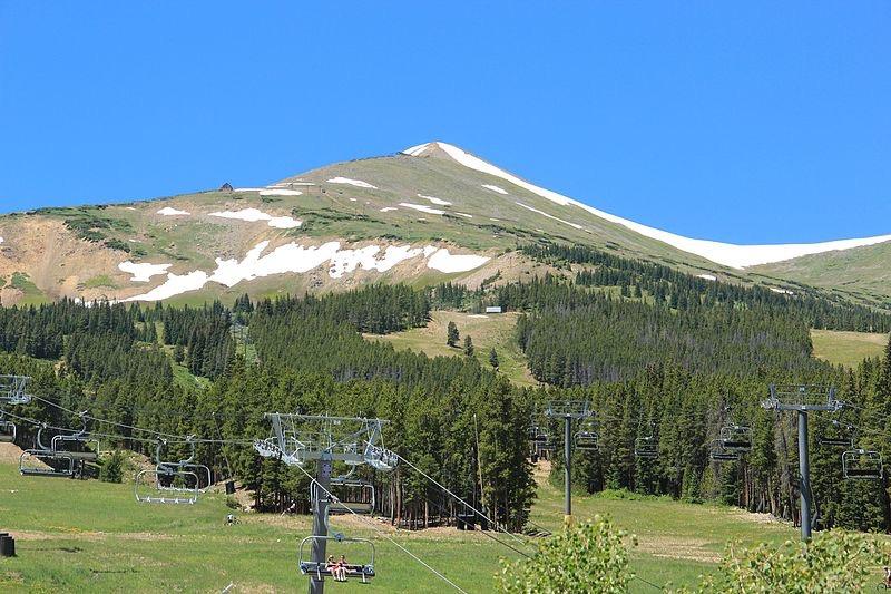 A mountain with snow patches and green slopes, featuring multiple ski lifts.