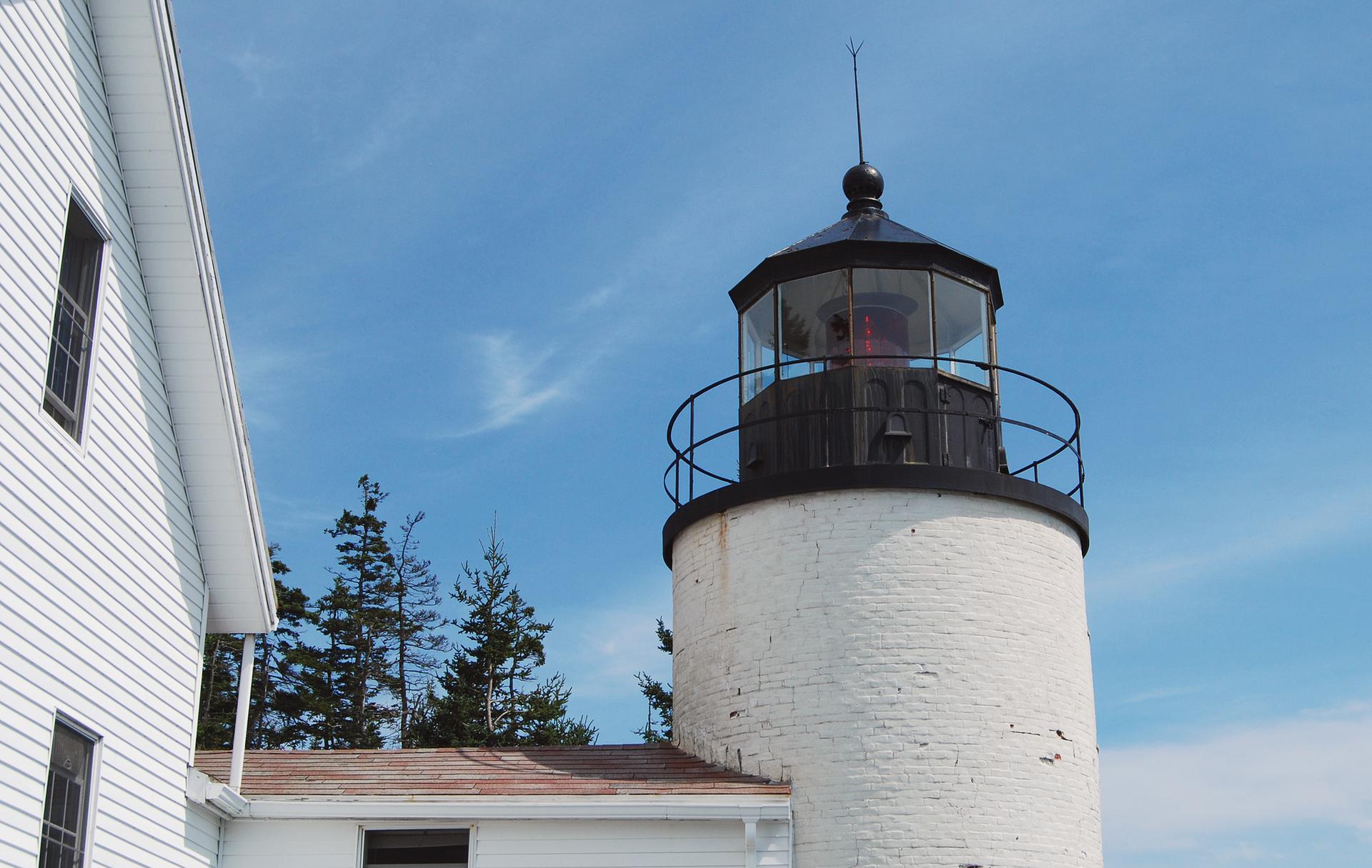 White lighthouse tower next to a white building under a clear blue sky.
