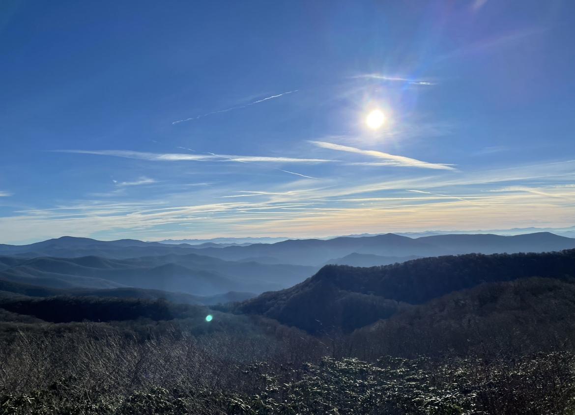Bright sun over a vast, hazy mountain landscape under a clear blue sky.