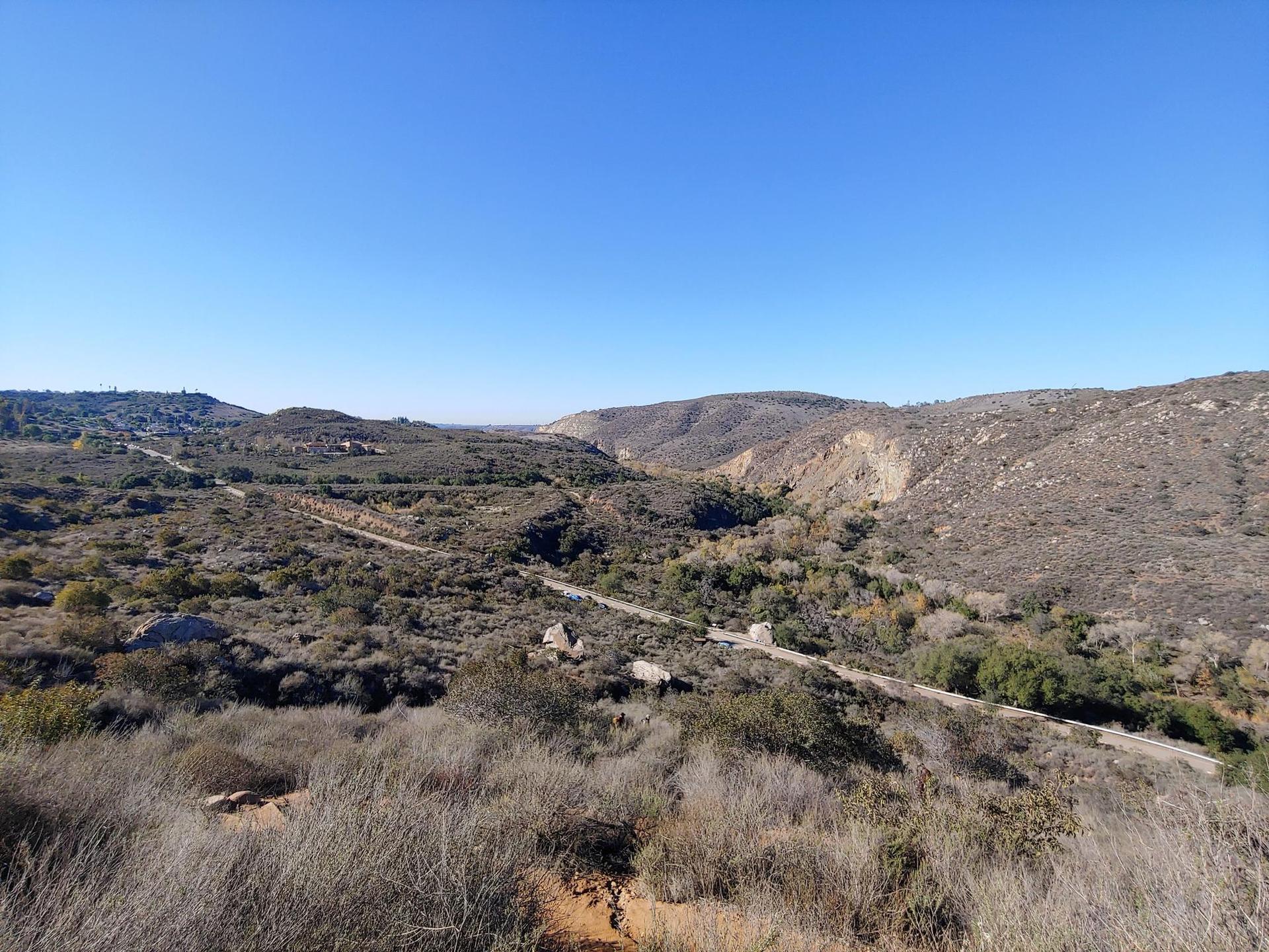 Expansive view of a dry, brushy valley with a dirt road under clear sky.