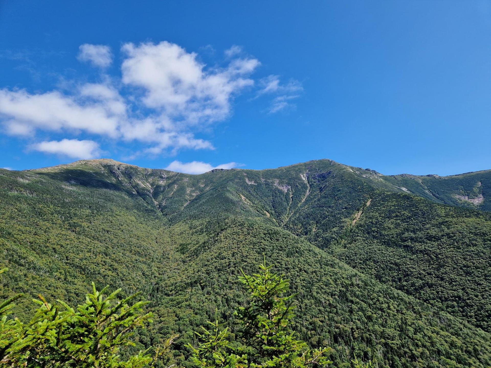 Lush green forested mountains under a bright blue sky with scattered clouds.