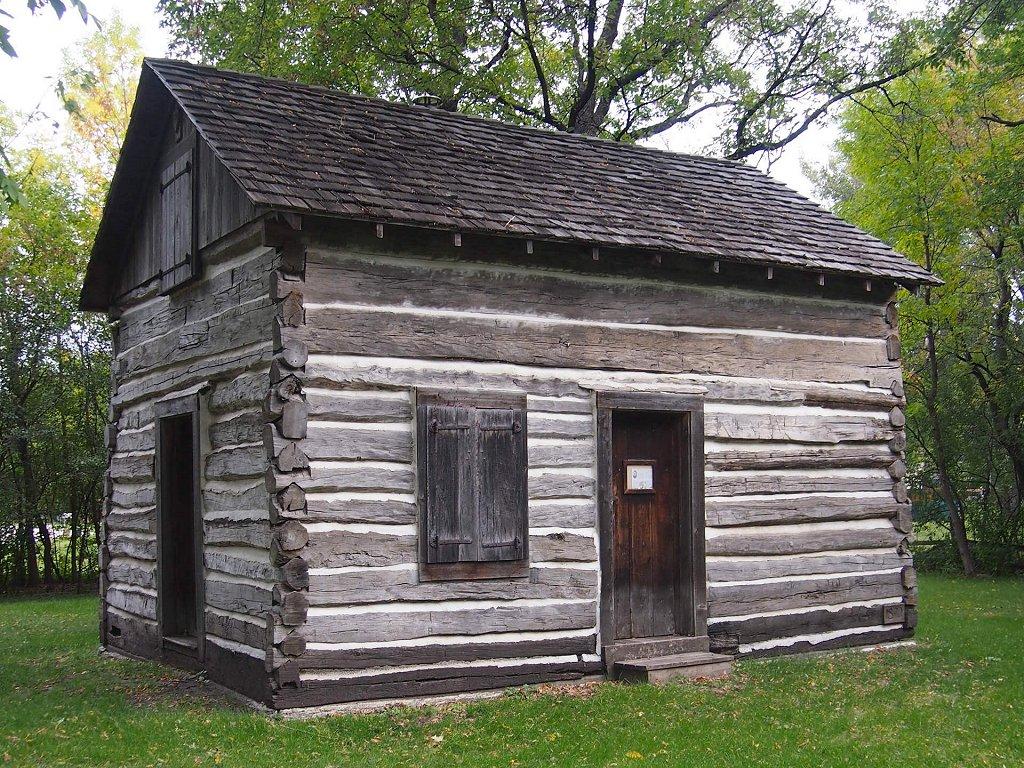 Rustic old log cabin with a wooden roof surrounded by green grass.