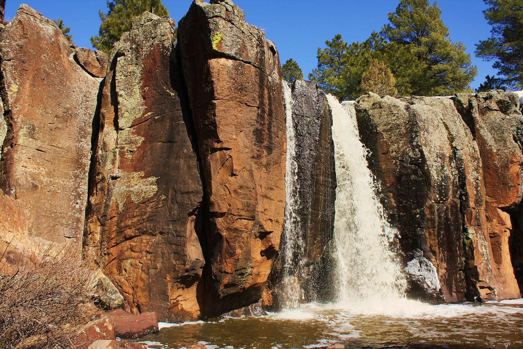 Waterfall cascading over dark red rock cliffs into a pool.