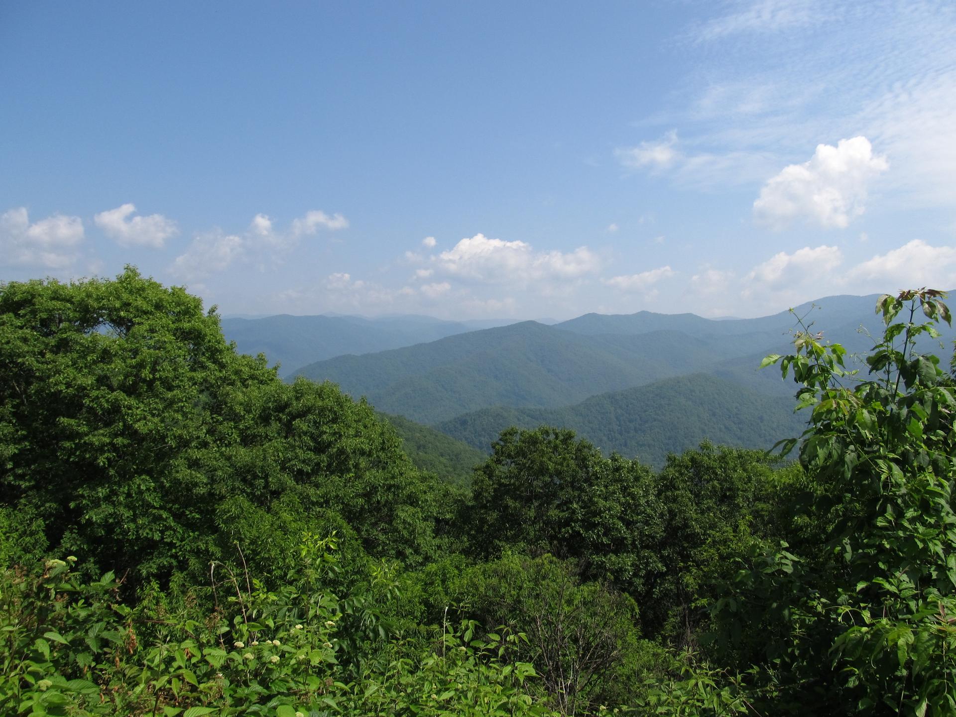 Vast green mountain landscape under a clear blue sky with scattered clouds.