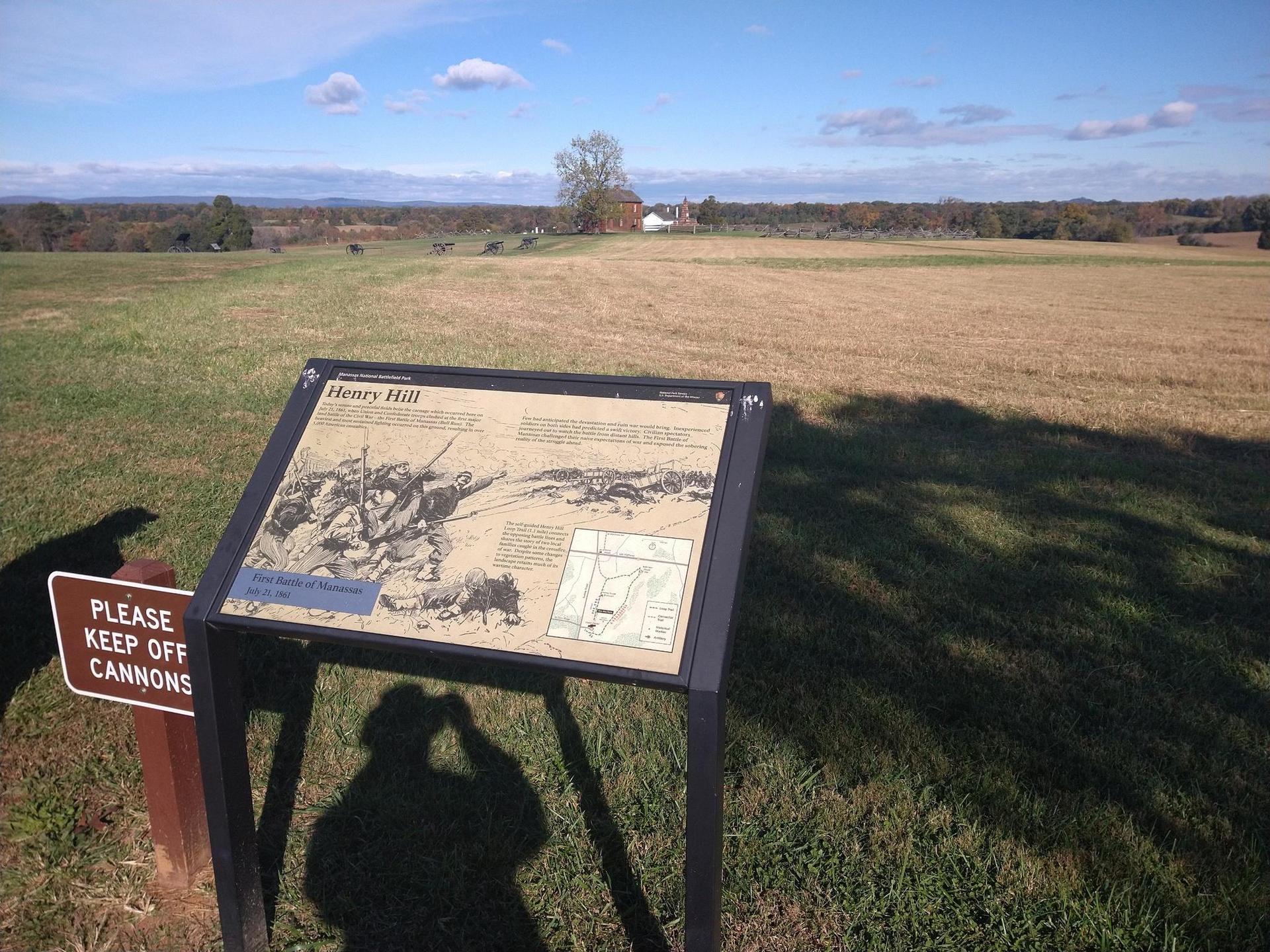 Interpretive sign in a grassy field with a distant house under a blue sky.