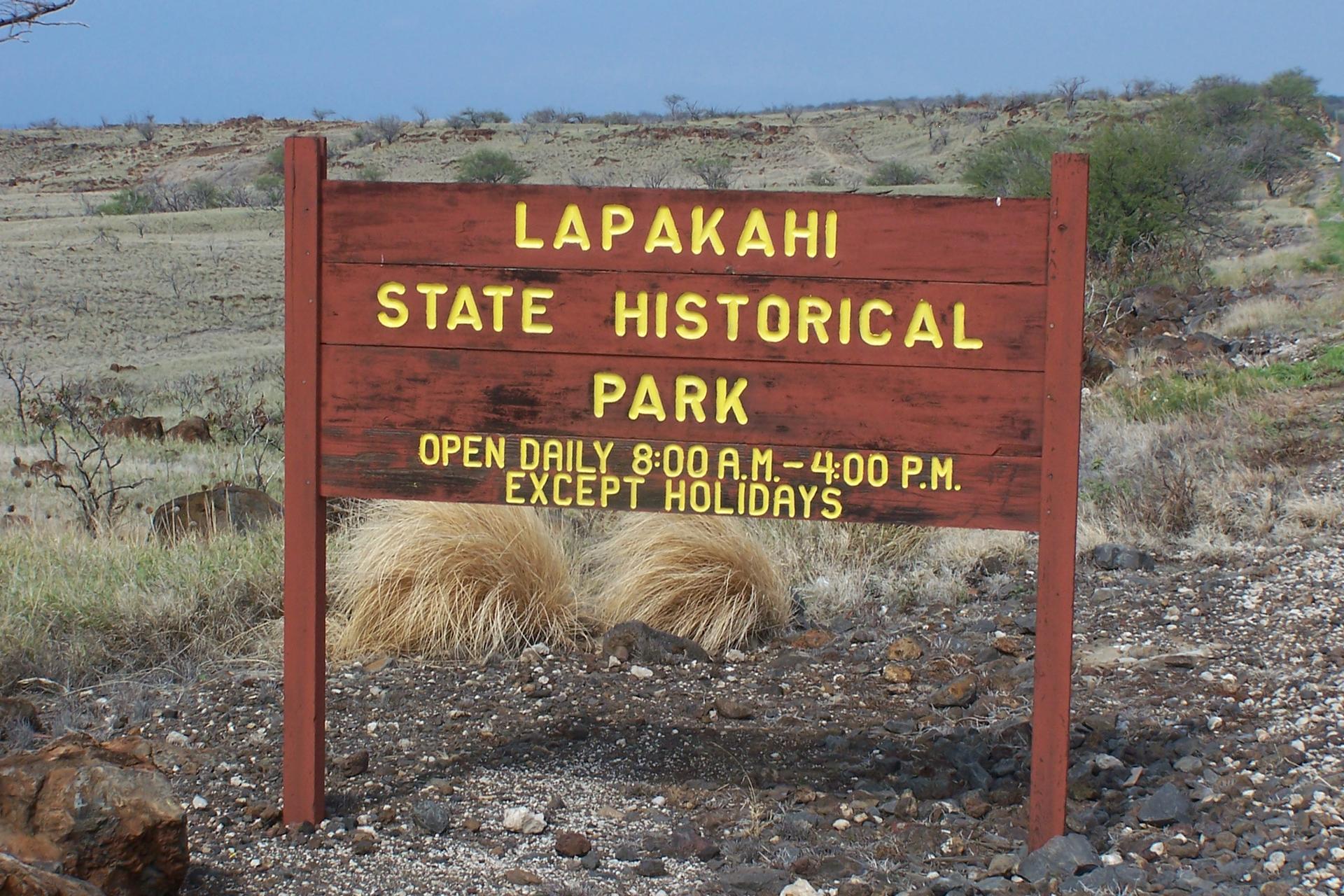 A weathered wooden sign stands in a dry, rocky landscape under a bright sky.