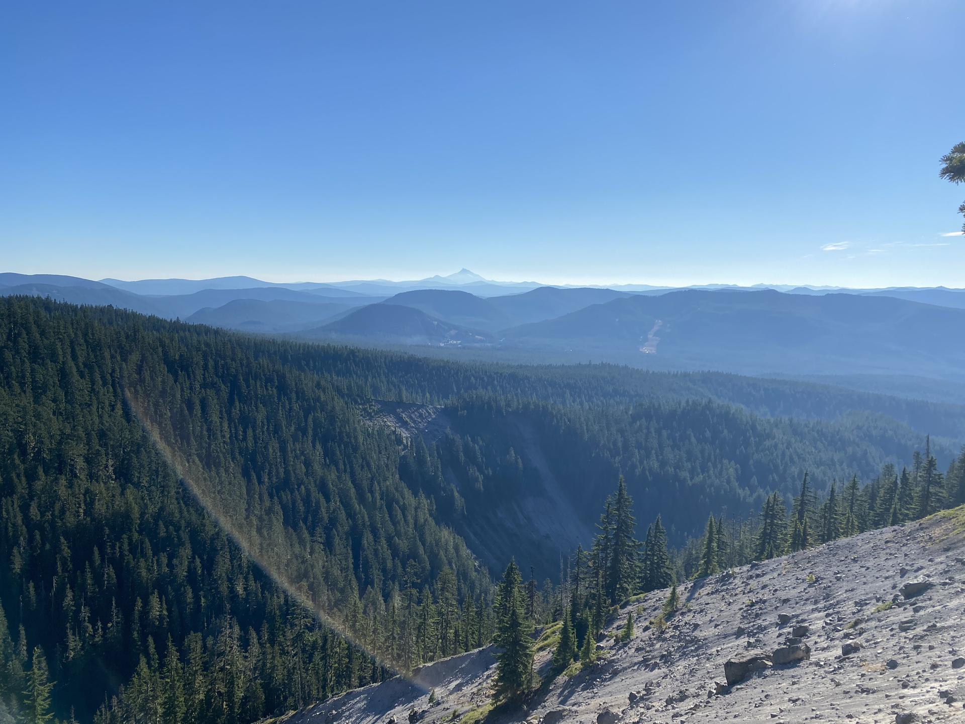 A vast forested mountain range stretches under a clear blue sky.