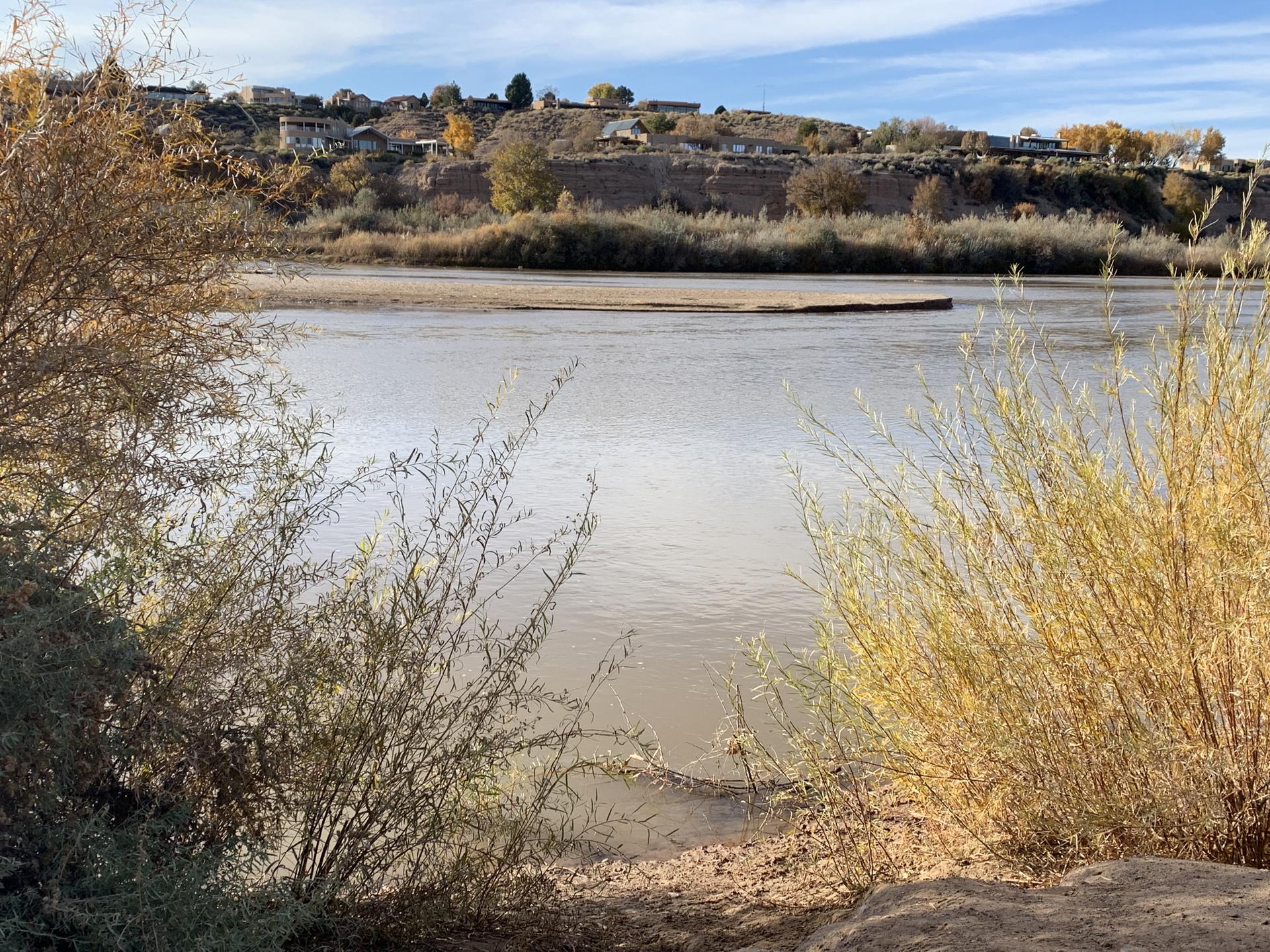 Wide river with a sandy bank, distant houses on a hill under clouds.