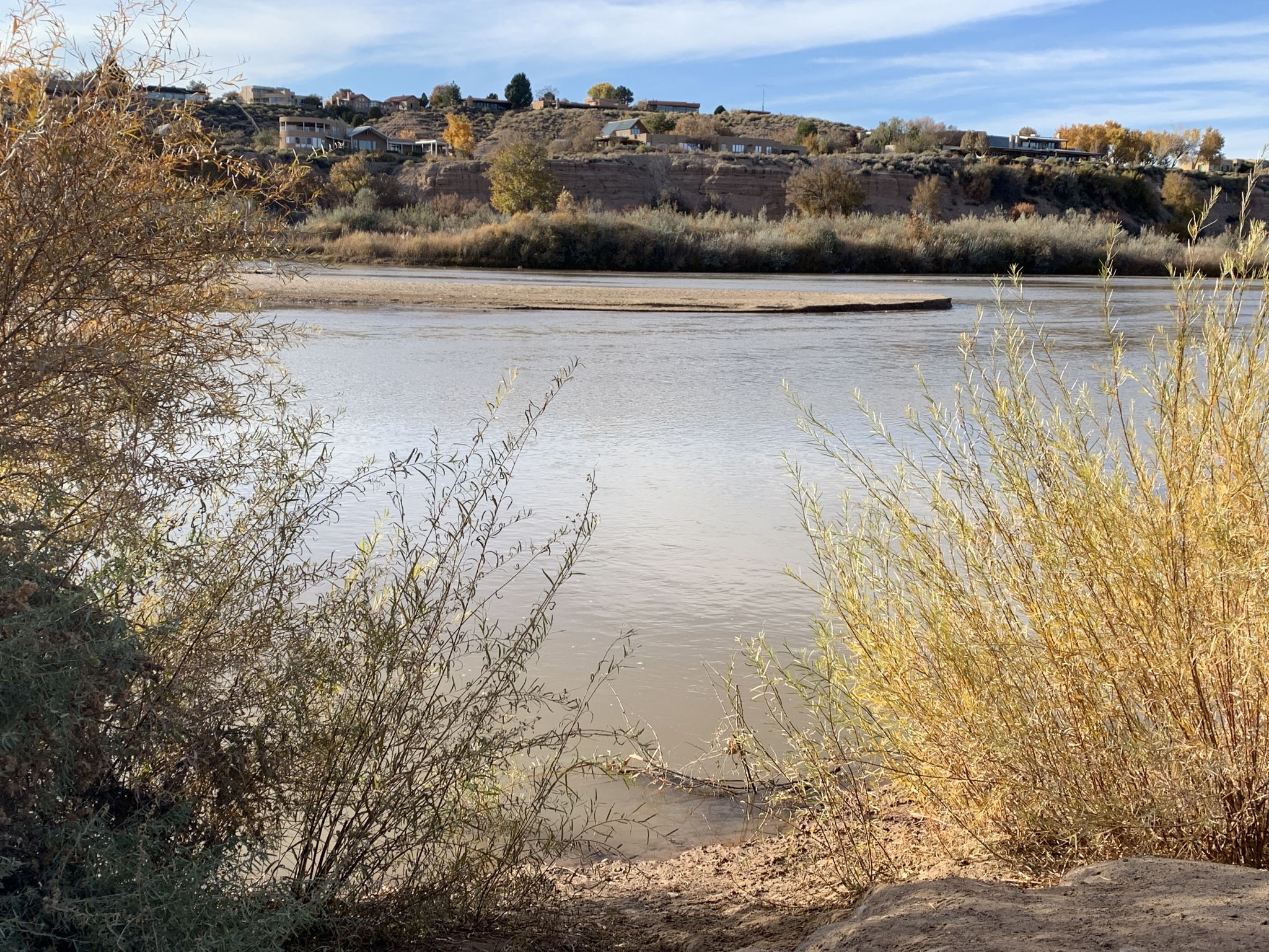 Wide river with a sandy bank, distant houses on a hill under clouds. - Paseo del Bosque Trail Loop