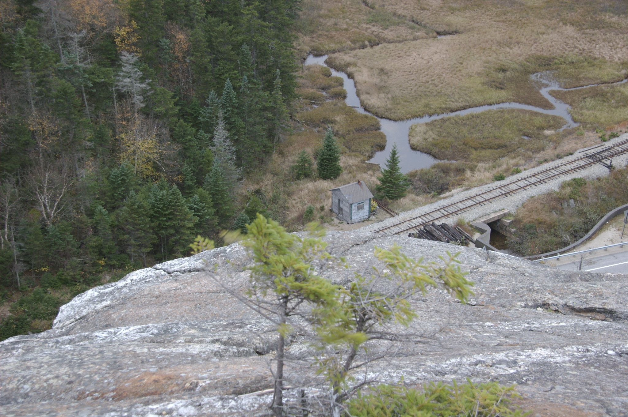 Rocky cliff overlooking a marshy valley with train tracks and a small building. - Elephant Head Spur